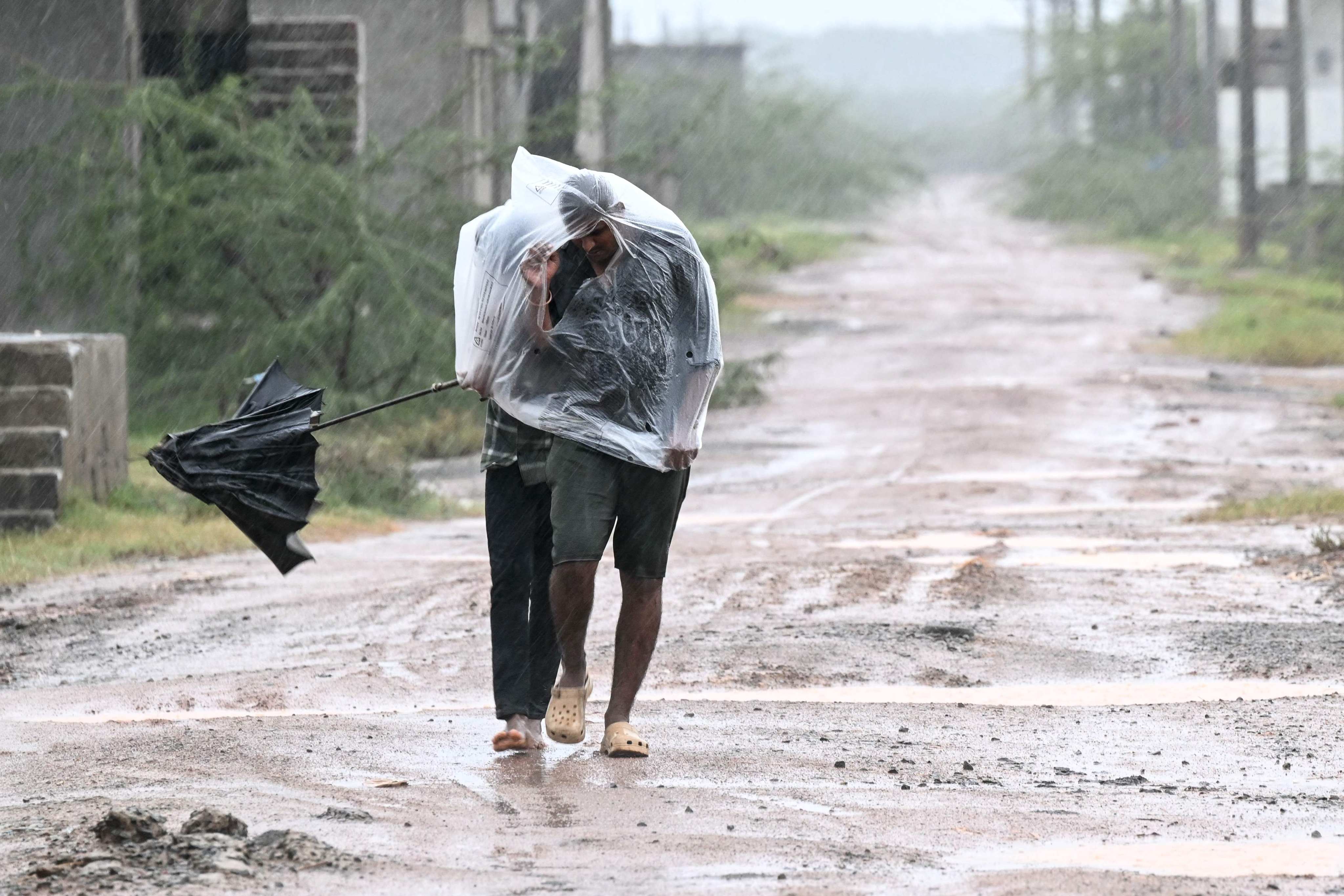 Men use a plastic sheet to cover themselves during rainfall in Andhra Pradesh’s Kakinada on Tuesday. Photo: AFP