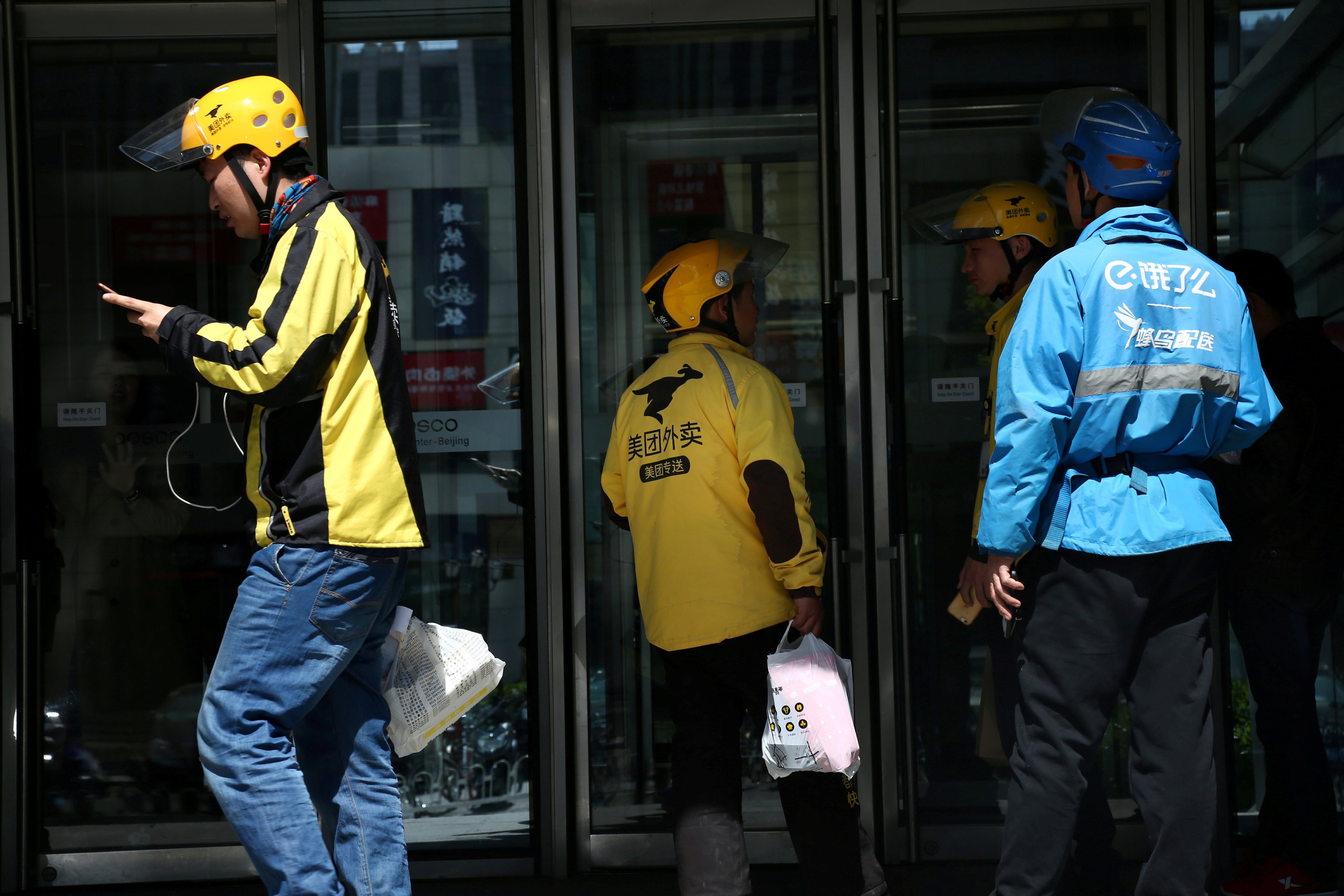 Drivers of on-demand food delivery services providers Ele.me, in blue, and Meituan Dianping, in yellow, are seen in Beijing on April 11, 2018. Photo: Reuters