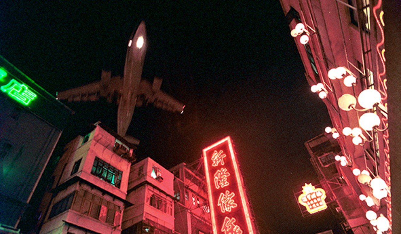 A plane appears over a neon-lit street in Kowloon City. Photo: Birdy Chu