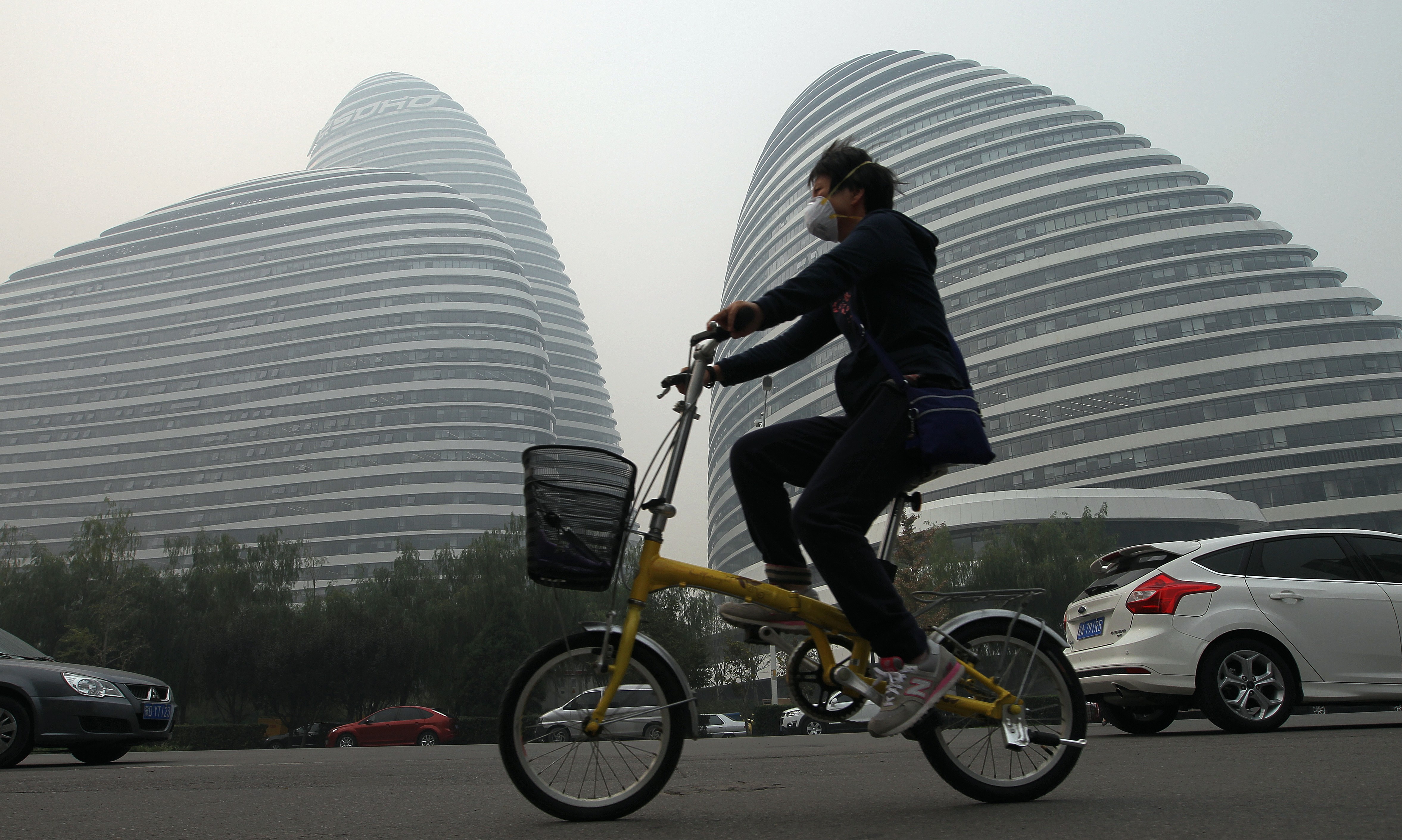 A woman wearing mask rides a bike passing by the Wangjing SOHO office towers in Beijing on October 9, 2014. The office towers, designed by Iraqi-British architect Zaha Hadid, is one of the biggest cash cows for their developer Soho China. Photo: SCMP/Simon Song