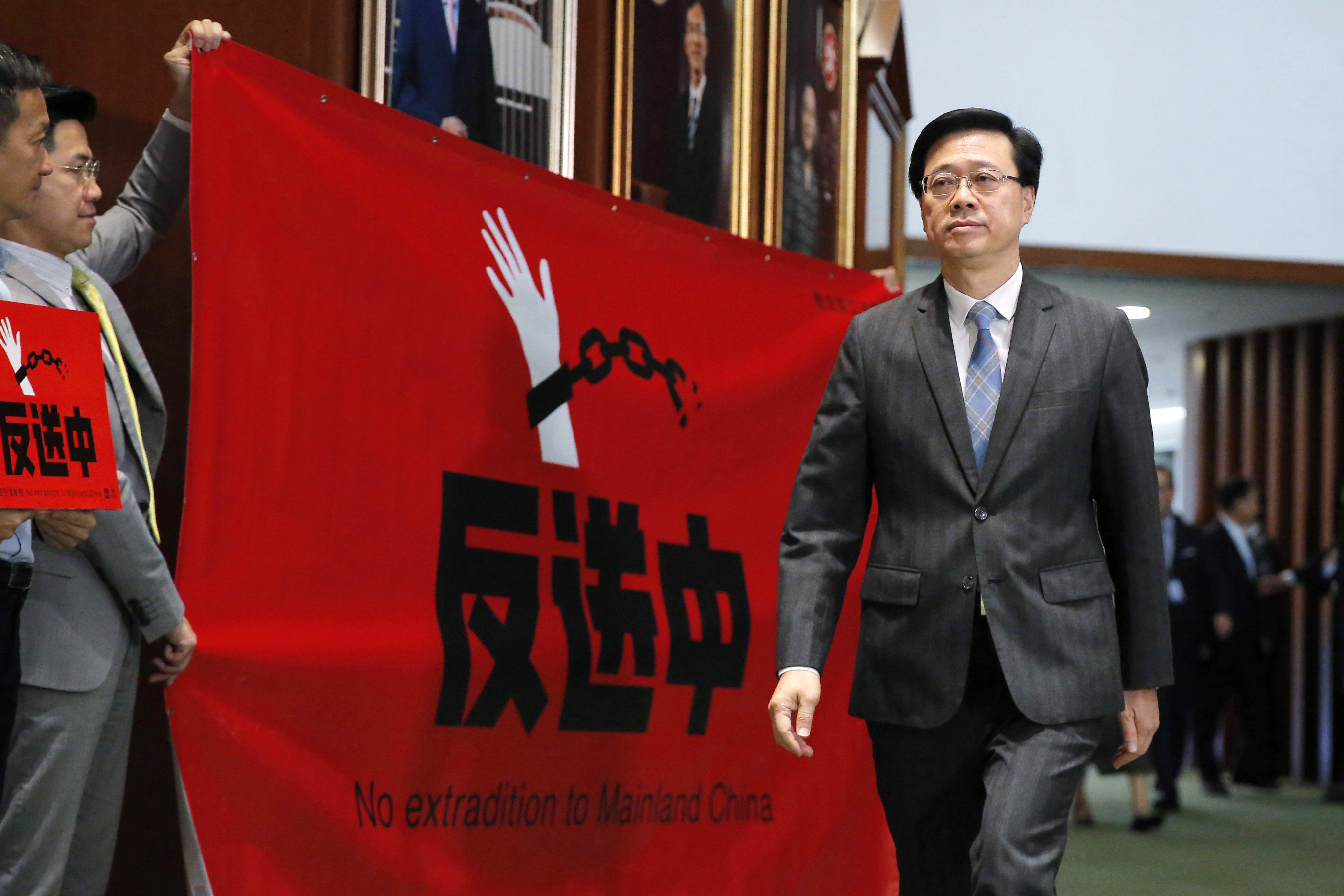 Secretary for Security John Lee Ka-chiu arrives for a meeting at the Legislative Council as pro-democracy lawmakers hold a placard and banner against the extradition bill, on May 22. Photo: AP