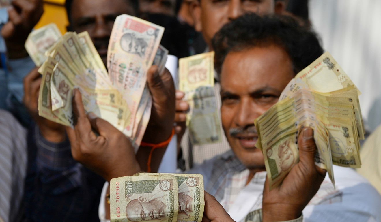 People waiting to exchange demonetised Indian currency, show their old 500 and 1,000 Rupee notes near the closed gates of the Reserve Bank of India in January 2017. Photo: AFP