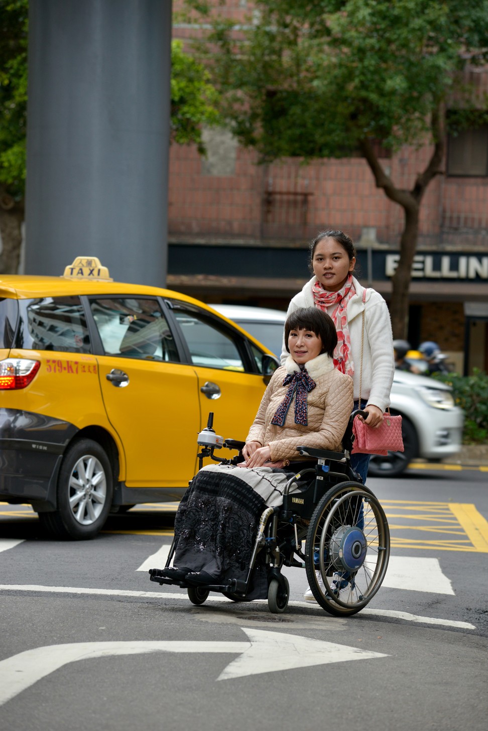 Yang’s assistant helps her cross a road in Taipei in her wheelchair. Photo: Chris Stowers