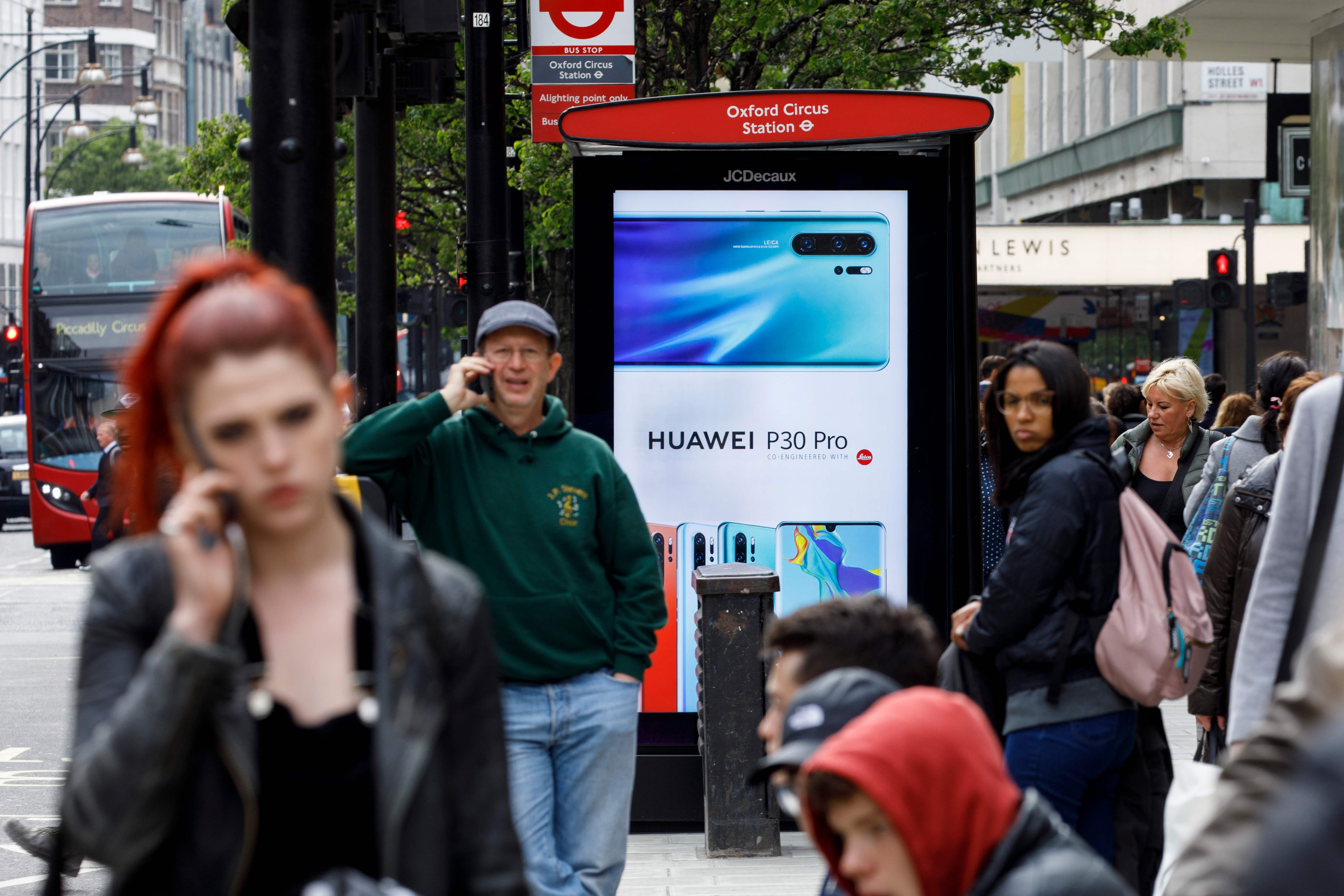 Pedestrians on their mobile phones near a Huawei advertisement at a bus stop in central London in April. Photo: AFP