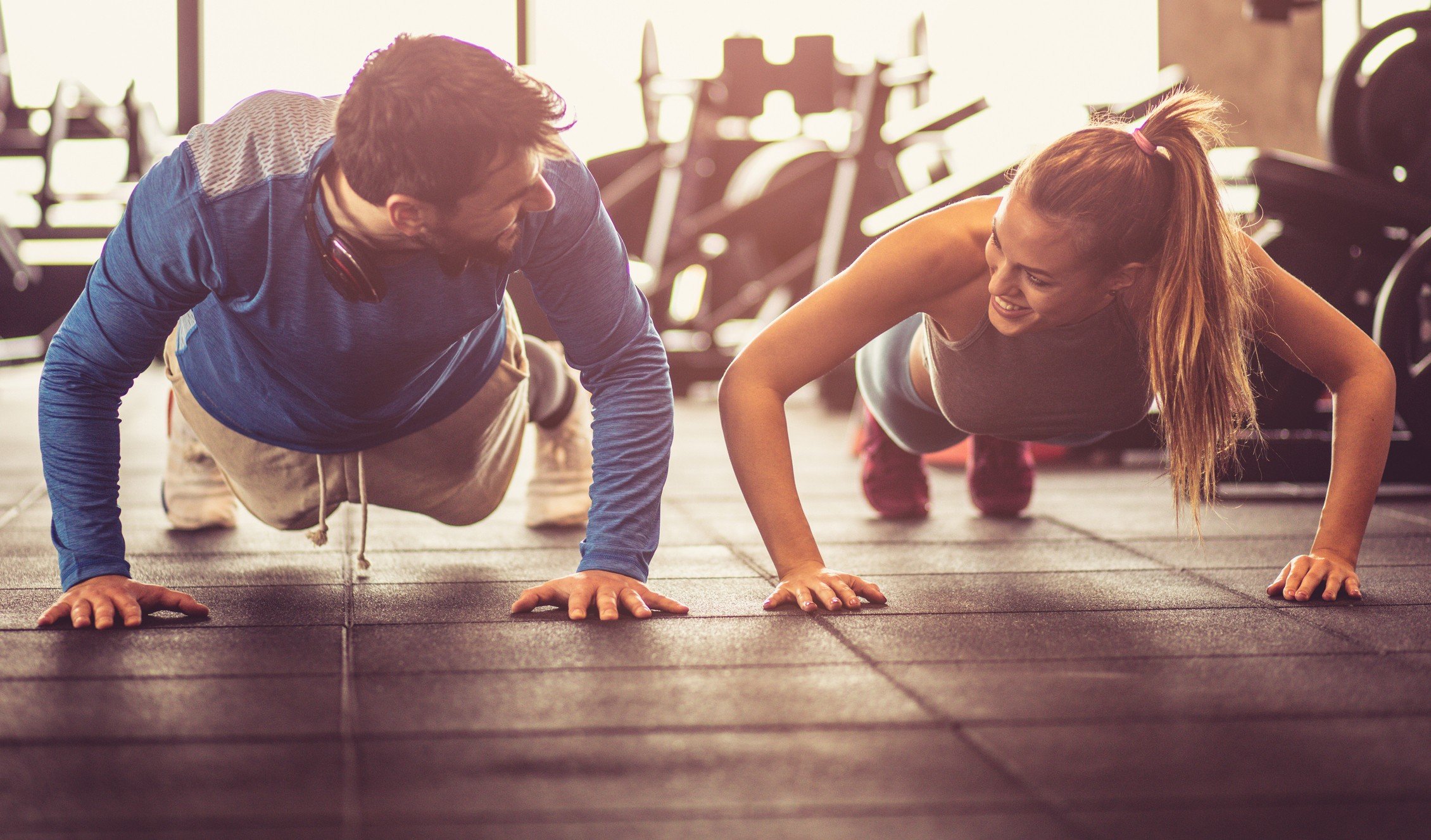 A young couple enjoy themselves while doing push-ups in a gym.
