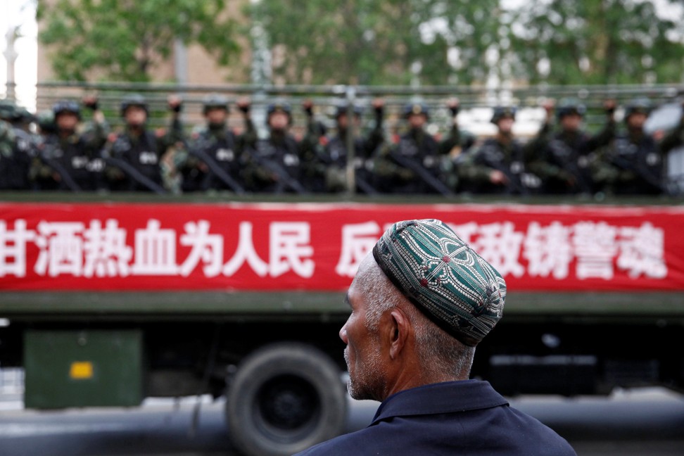 A Uygur man looks on as a truck carrying paramilitary policemen travels along a street during an anti-terrorism oath-taking rally in Urumqi, Xinjiang, in May 2014. The Chinese characters on the banner read, “Willingness to spill blood for the people. Countering terrorism and fighting the enemies is part of the police spirit”. Photo: Reuters