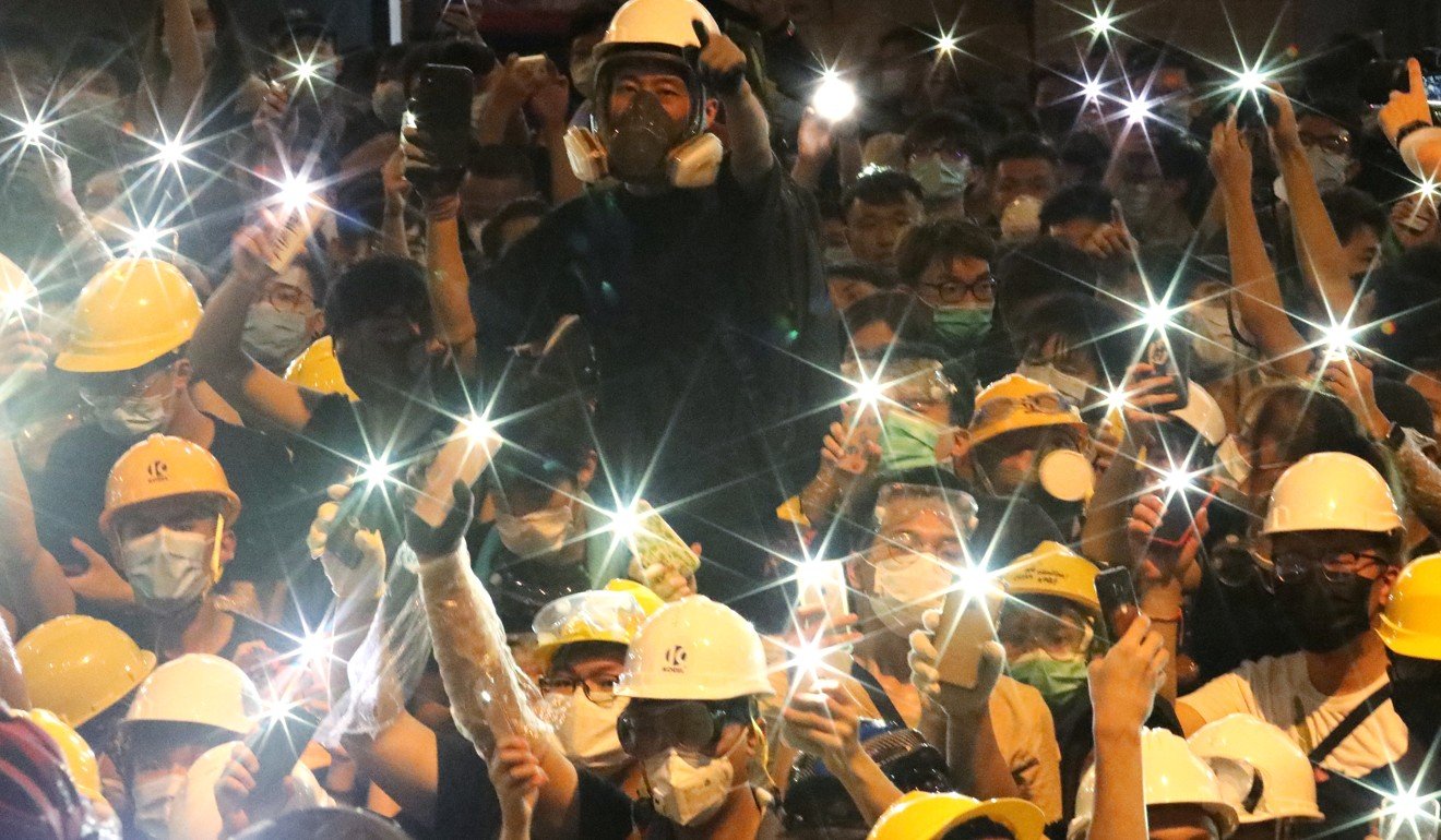 Protesters use flashlights on their mobile phones to shine into police headquarters as crowds surround the complex in a 15-hour stand-off. Photo: Felix Wong