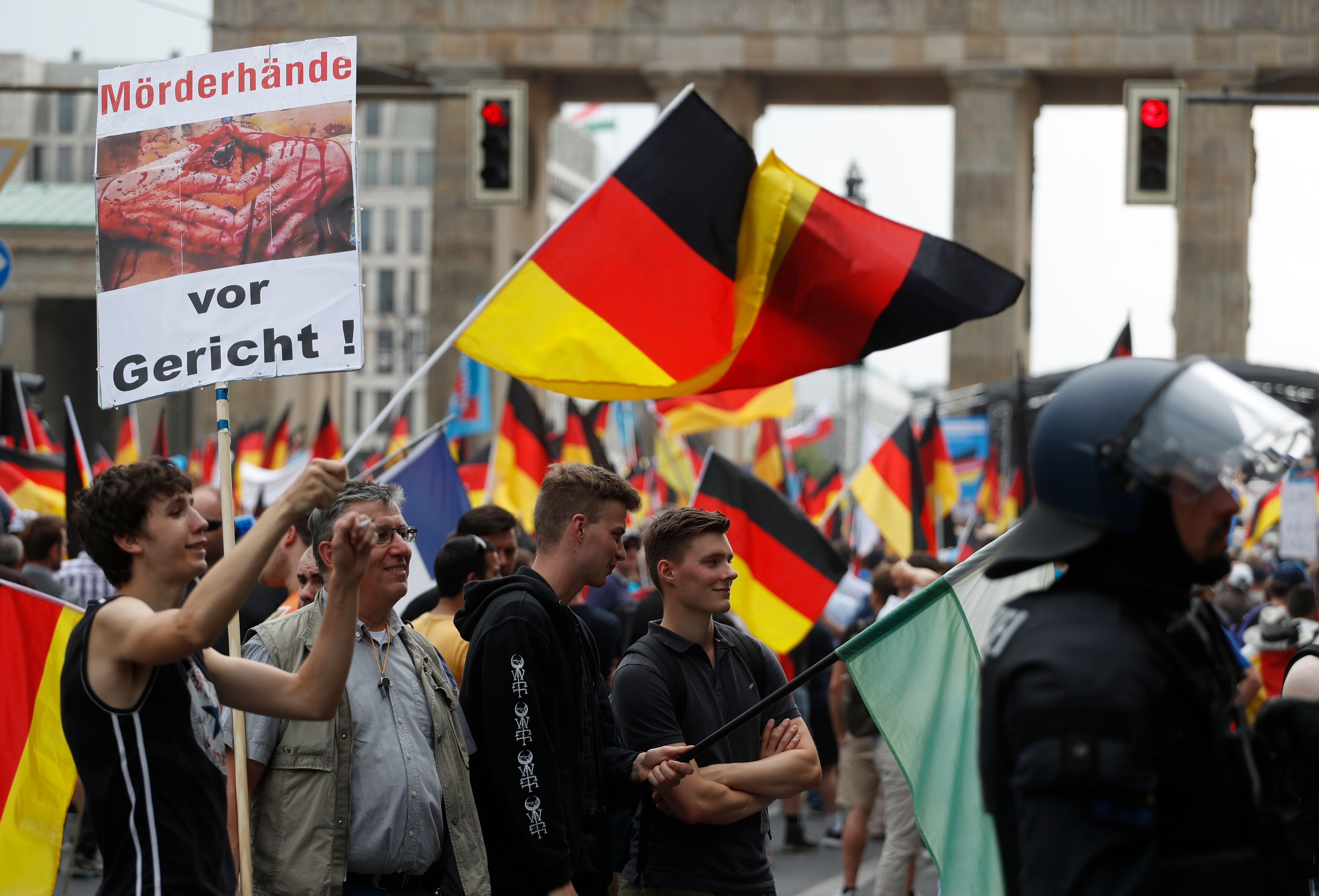 Alternative for Germany (AfD) demonstrators wave German flags and hold a placard reading ‘Killer’s hands in trial!’ in front of the Brandenburg Gate in Berlin. Photo: AFP