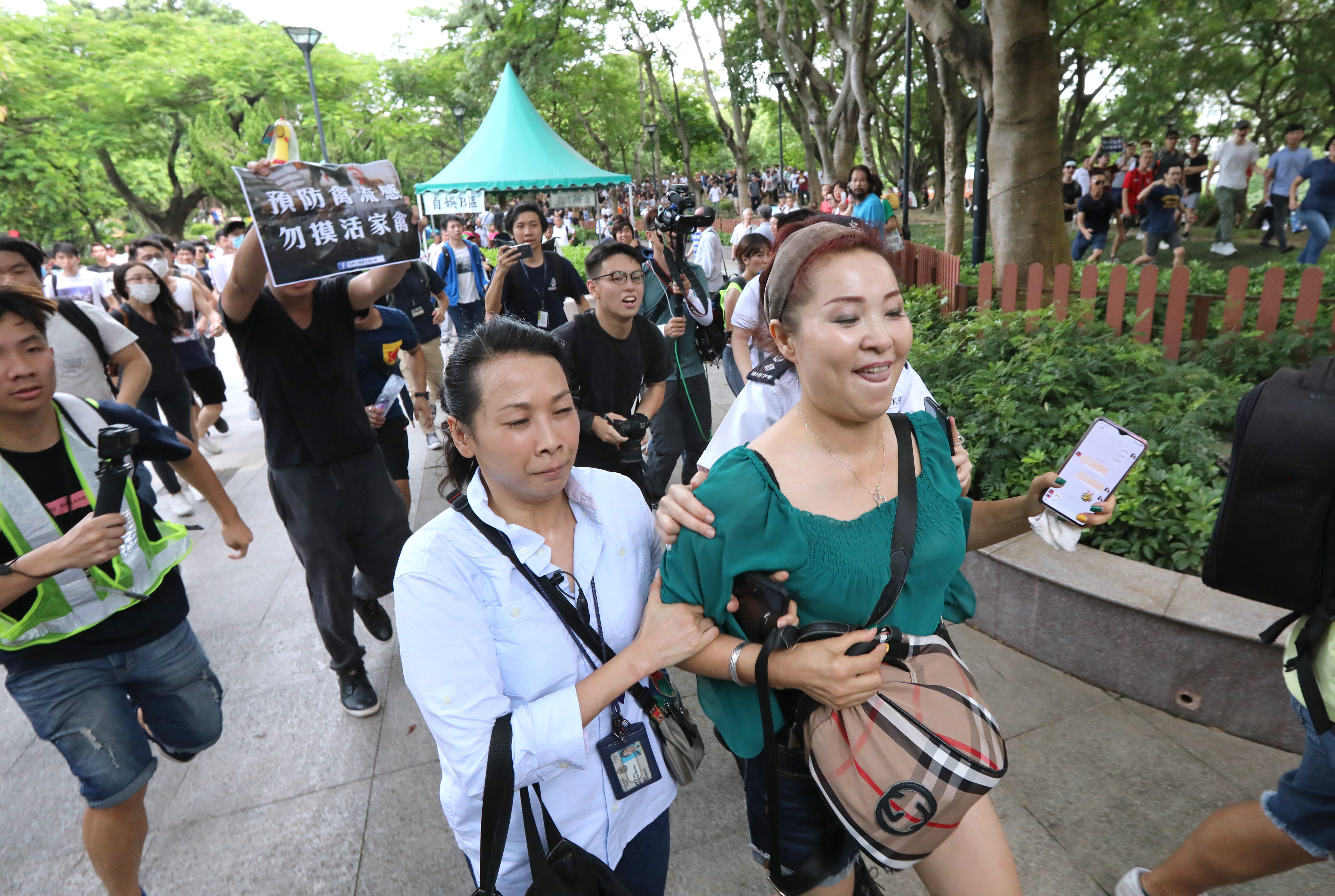 An officer escorts a woman away from angry protesters in Tuen Mun Park who are decrying niosy and indecent performances by ‘dama’ entertainers, mostly mainlanders. Photo: Felix Wong
