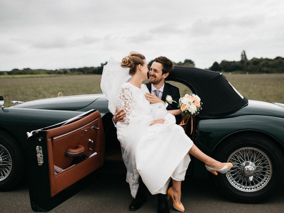 A bride and groom sit in a vintage sports car on their wedding day. Photo: Unsplash