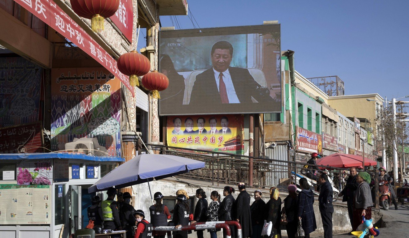 Residents queue at a security checkpoint beneath a screen showing Chinese President Xi Jinping, in Hotan, Xinjiang. Photo: AP