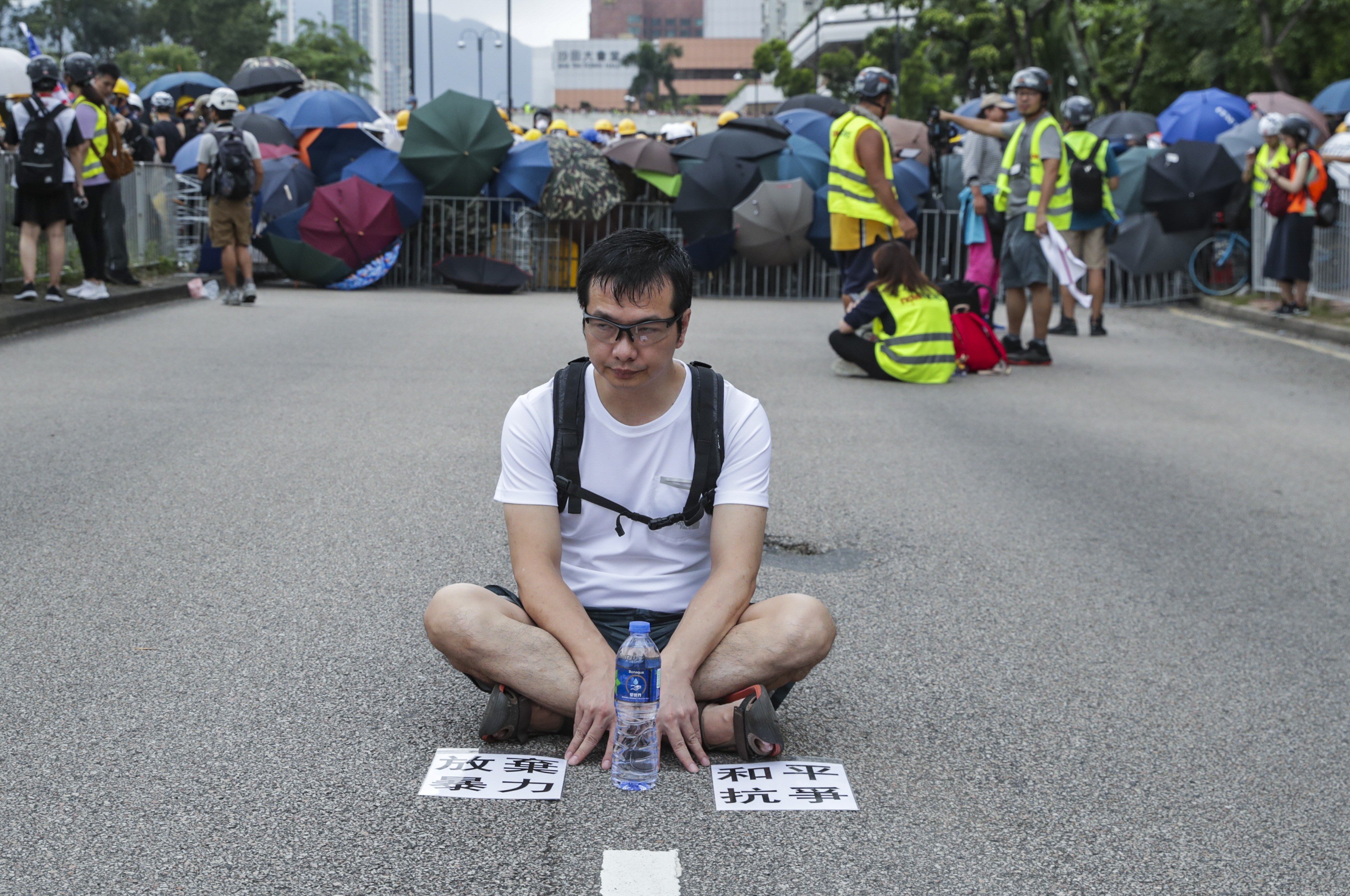 A protester sits down on a Sha Tin street to make a point about non-violence, during a rally against the now-shelved extradition bill, on July 14. The posters on the ground call on demonstrators to give up violence and protest peacefully. Photo: Edmond So