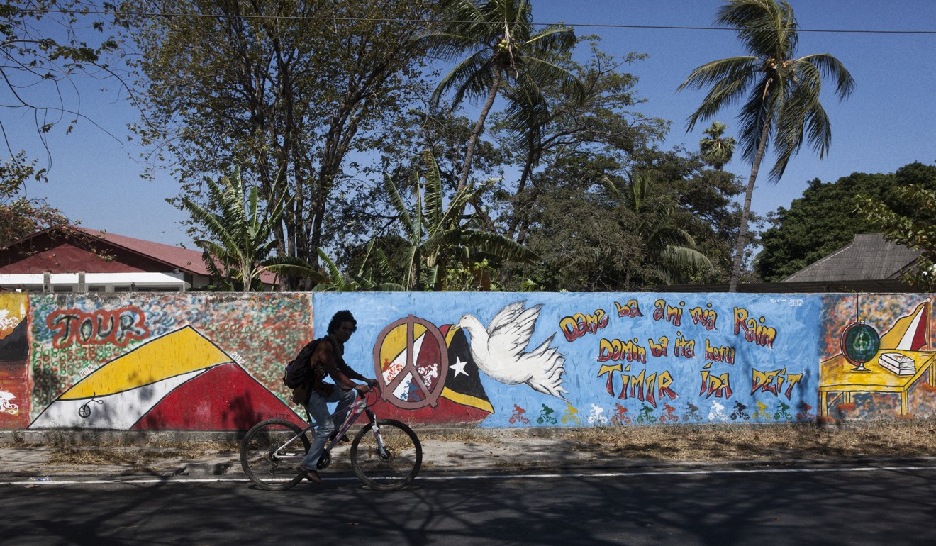 Seorang pria muda bersepeda melewati mural yang mempromosikan perdamaian di Dili tengah.  Foto: SCMP