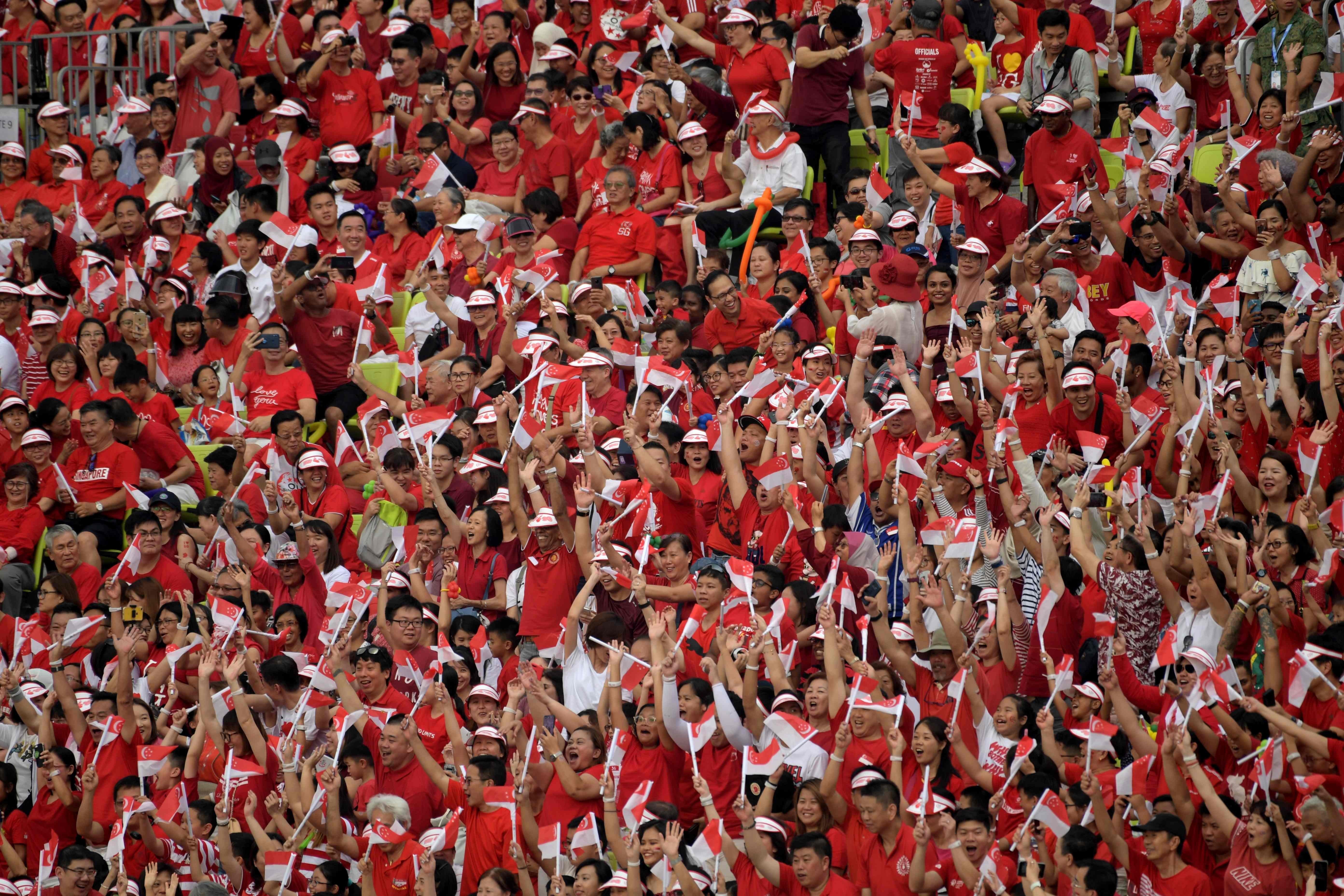 Spectators wave the Singapore national flag as they wait for the start of the 54th national day parade on Friday. Photo: AFP