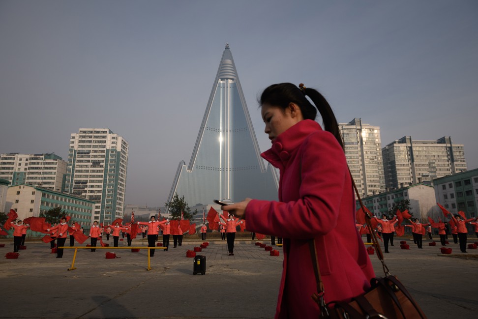A pedestrian checks her mobile phone as she passes members of a Socialist Women’s Union propaganda troupe performing a dance routine in front of the Ryugyong Hotel. Photo: AFP