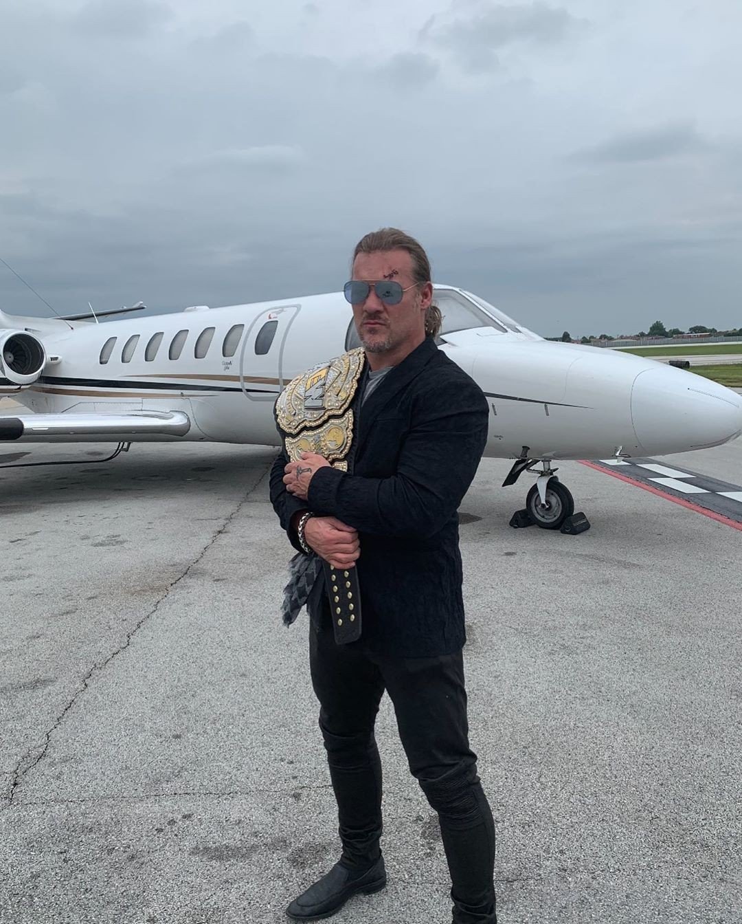 Chris Jericho poses with the AEW world title belt outside a private jet. Photo: Instagram/Chris Jericho