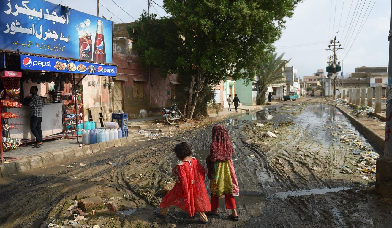 Children cross a muddy street wet from drainage and rainwater in Karachi. Photo: AFP