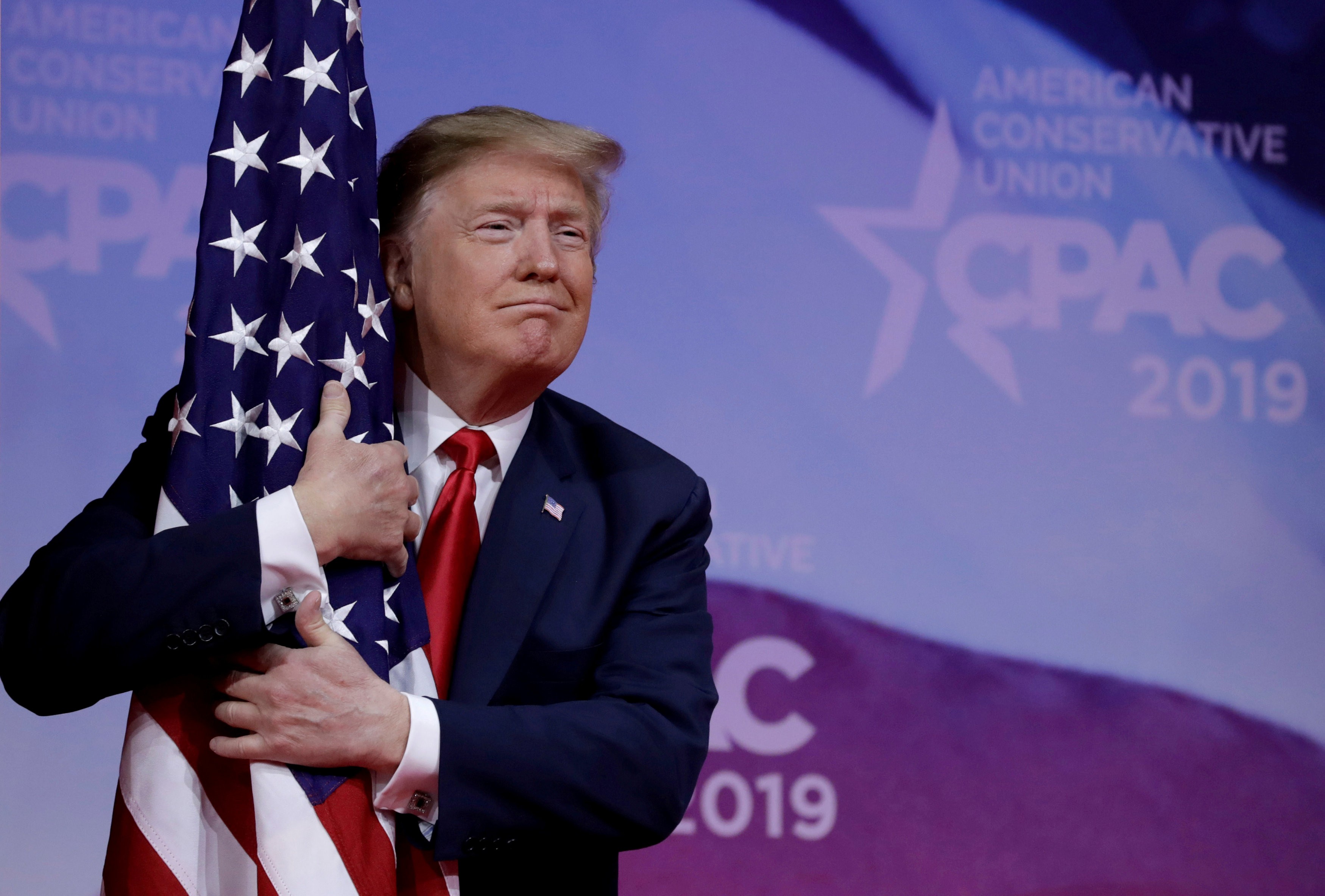 US President Donald Trump hugs the American flag at the Conservative Political Action Conference annual meeting near Washington on March 2. Photo: Reuters