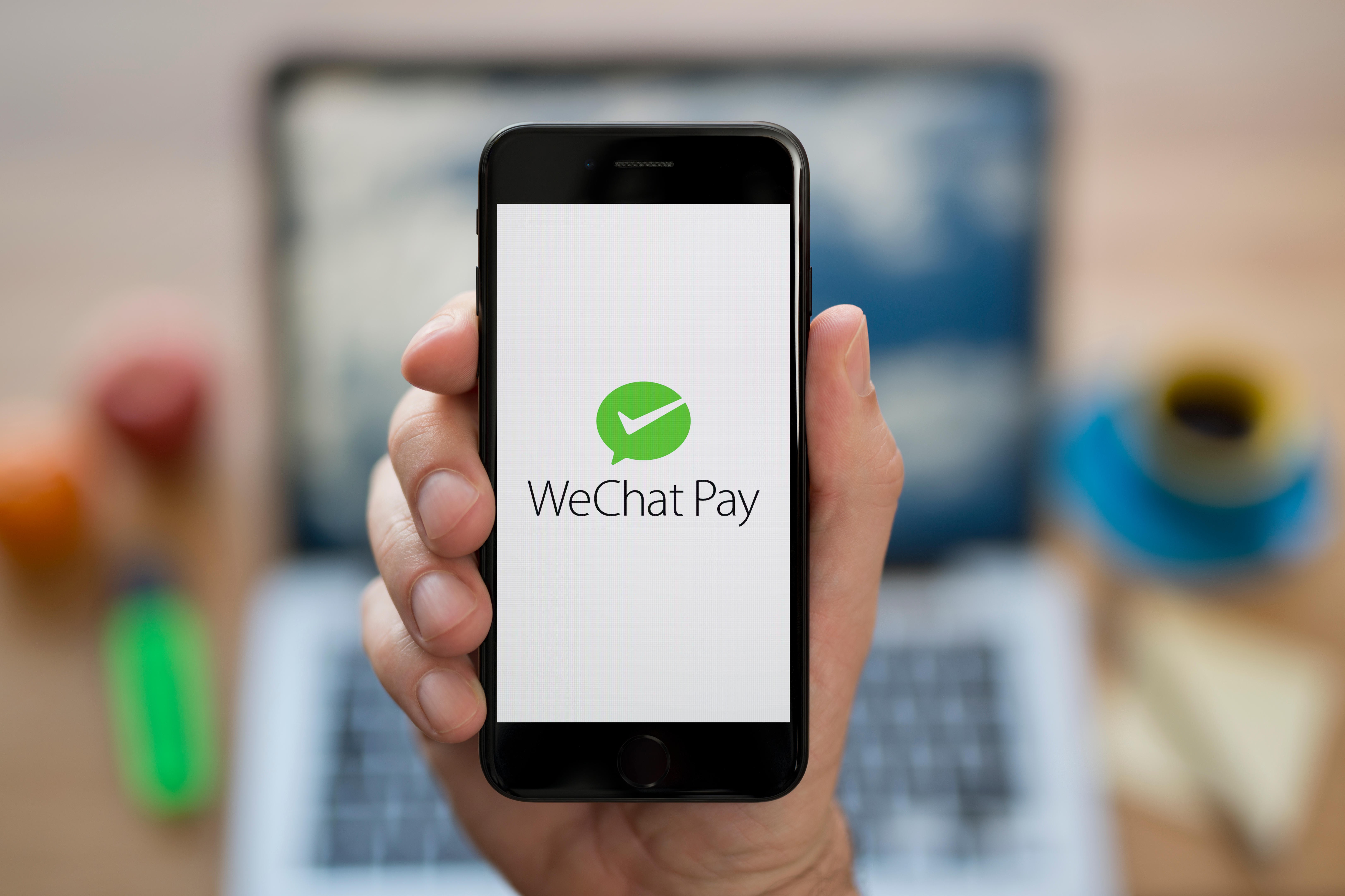 A man looks at his iPhone which displays the WeChat Pay logo, while sat at his computer desk. Photo: SCMP
