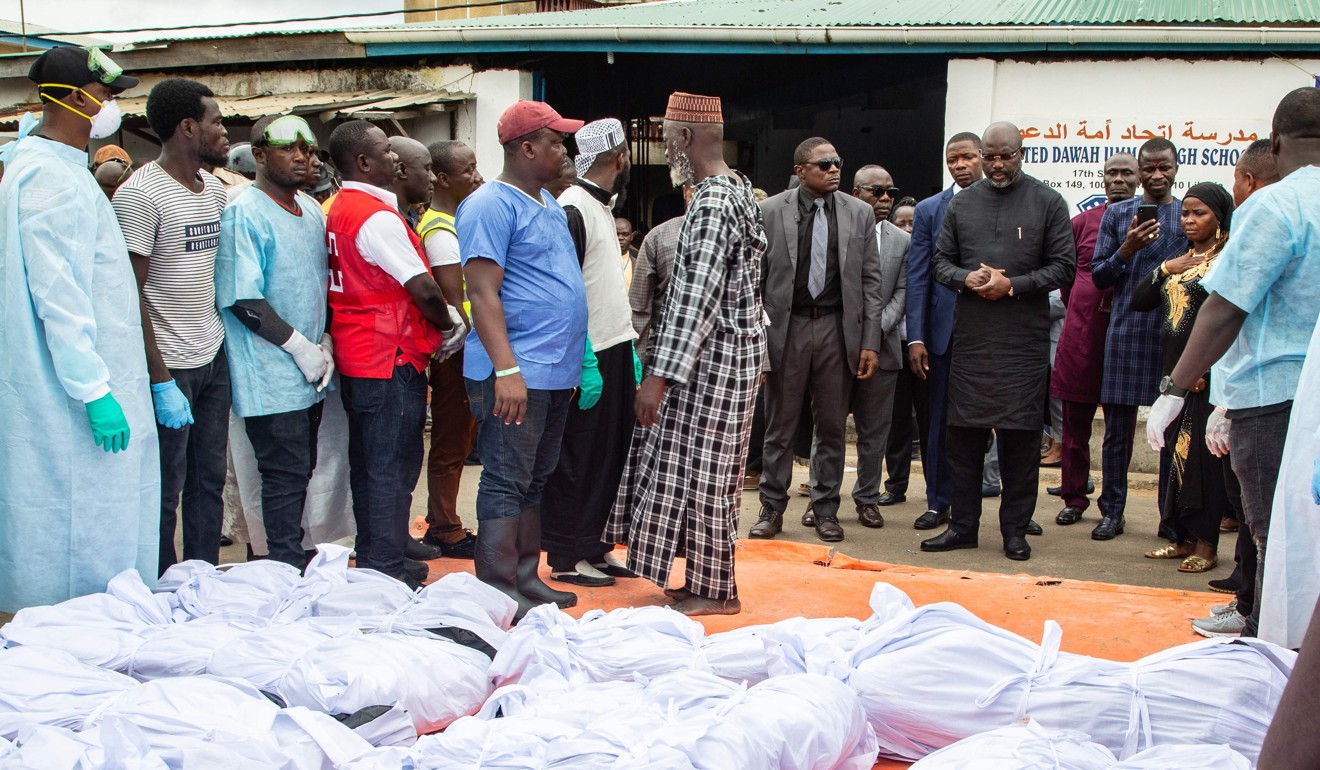 Liberian President George Weah pays his respects and he stands in front of the bodies. Photo: AFP