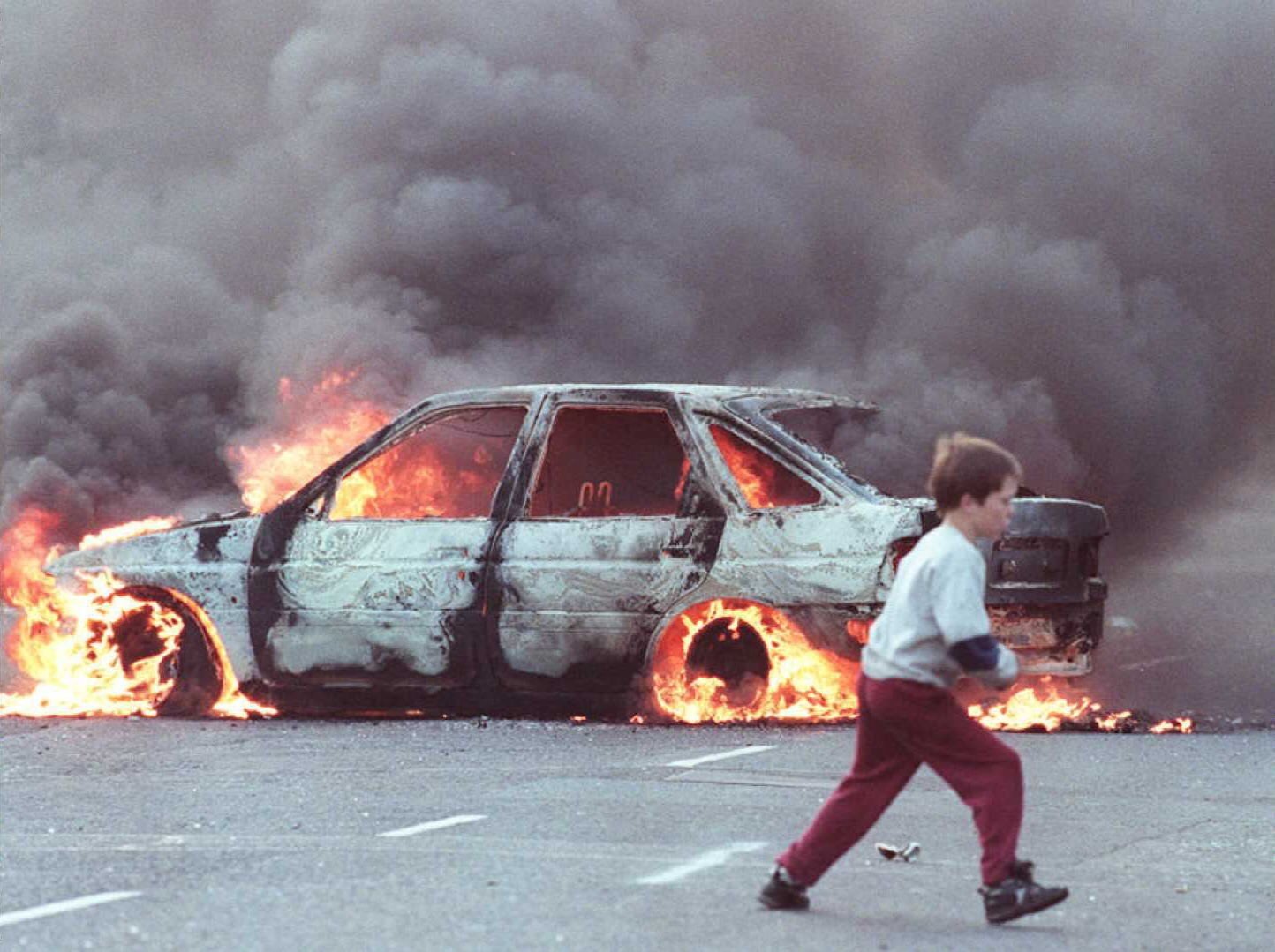 A boy runs past a burning car in the Catholic area of Shortstrand during the Troubles in Belfast, Northern Ireland in July 1996. Photo: AFP