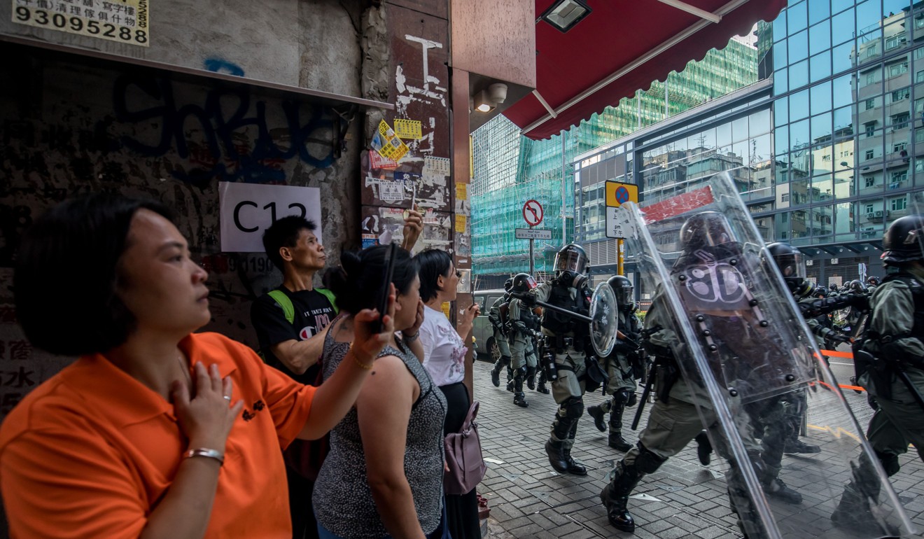 Pedestrians hold up smartphones as riot police advance along a street during a protest in the Sham Shui Po district of Hong Kong, China, on Tuesday. Photo: Bloomberg