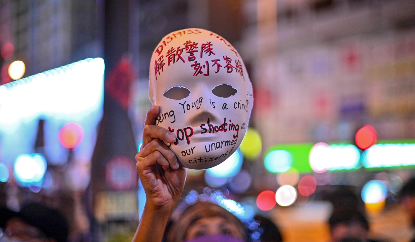 A woman holds a mask with slogans written on as protesters gather outside Mong Kok Police Station on Saturday night. Photo: AFP