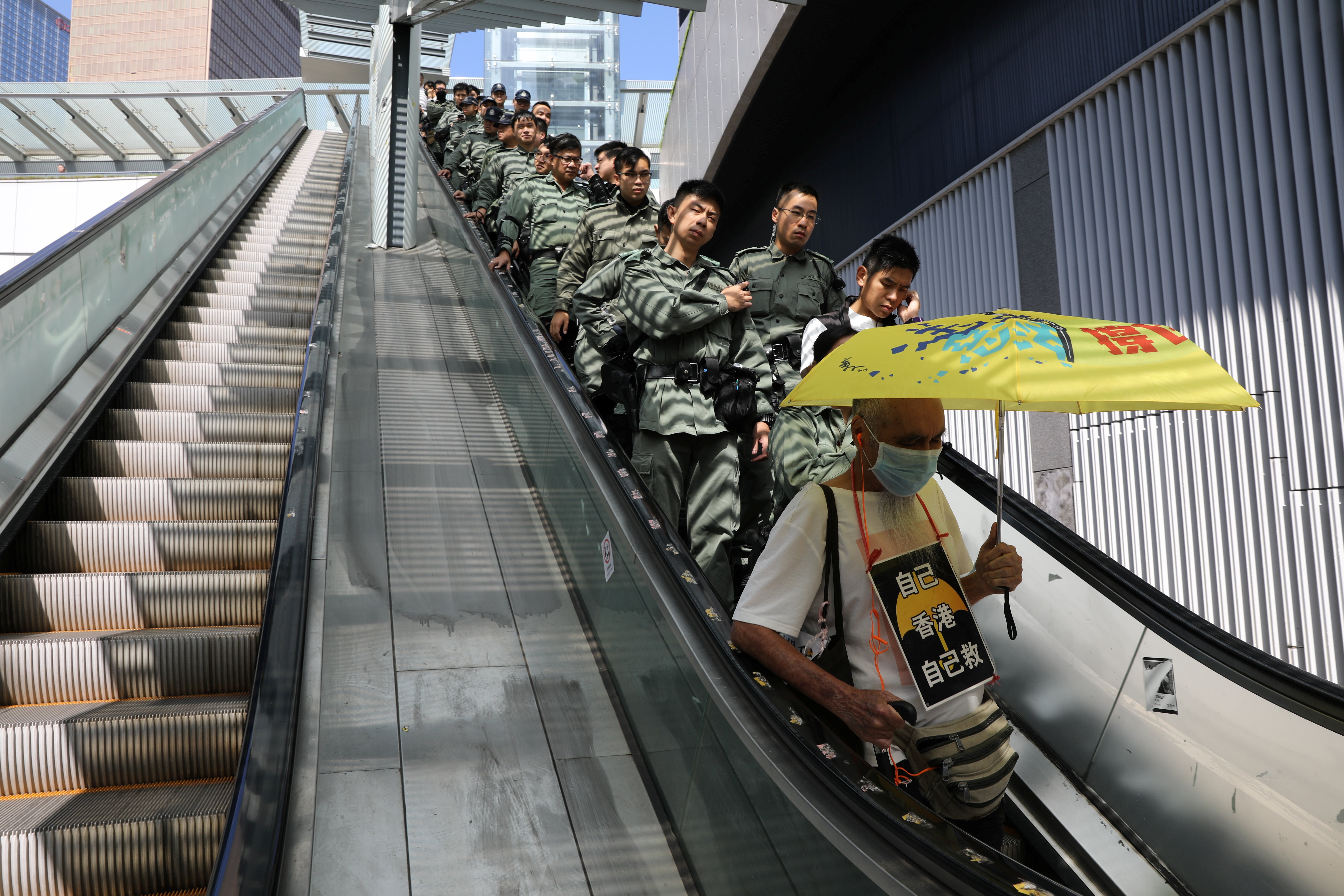 A line of police officers ride an escalator at the Legislative Council on October 16, behind a protester holding an umbrella. Photo: Reuters