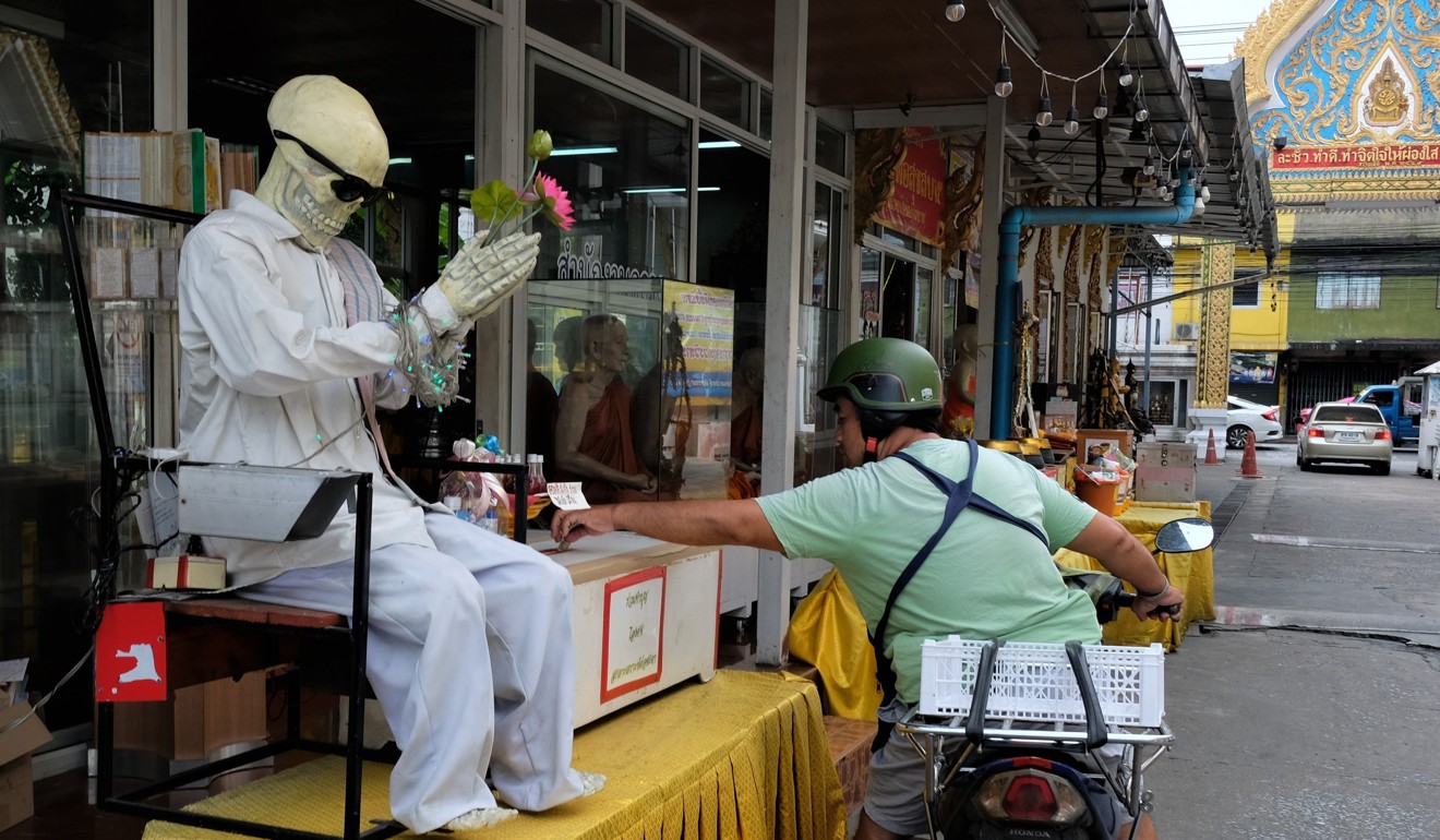 A man passing by on a motorcycle stops to donate to a Buddhist temple by a plastic automaton skeleton. A dread of malevolent spirits runs deep in Thailand. Photo: SCMP