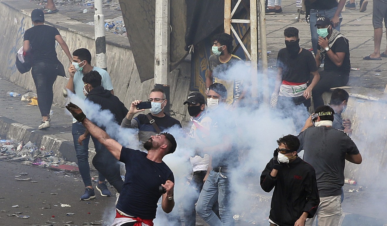 An anti-government protester throws a tear gas canister fired by Iraqi security forces. Photo: AP