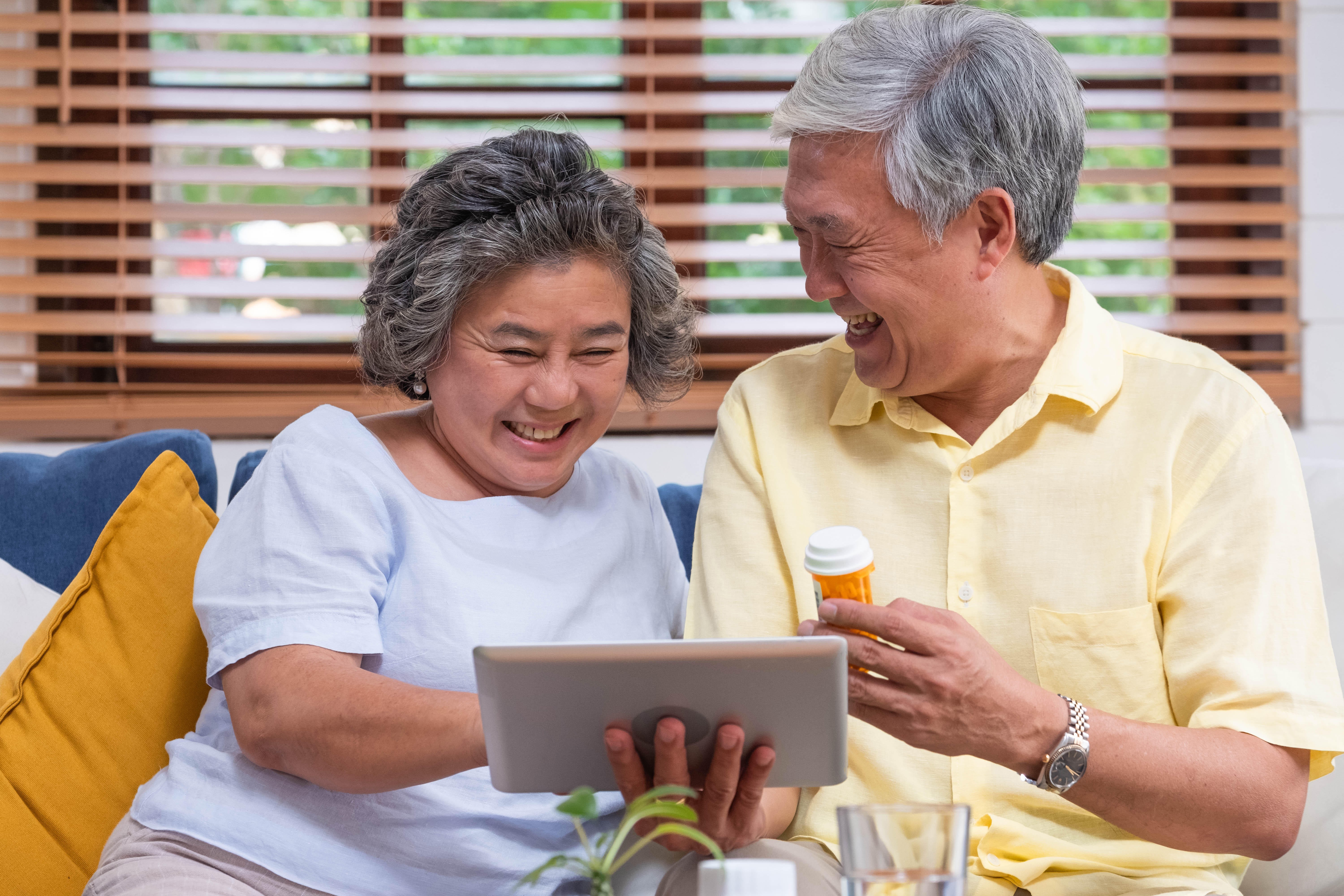 RR8A5A Asian senior couple use tablet video conference with doctor about pill while sitting on sofa at home,senior learn to use technology.aging at home