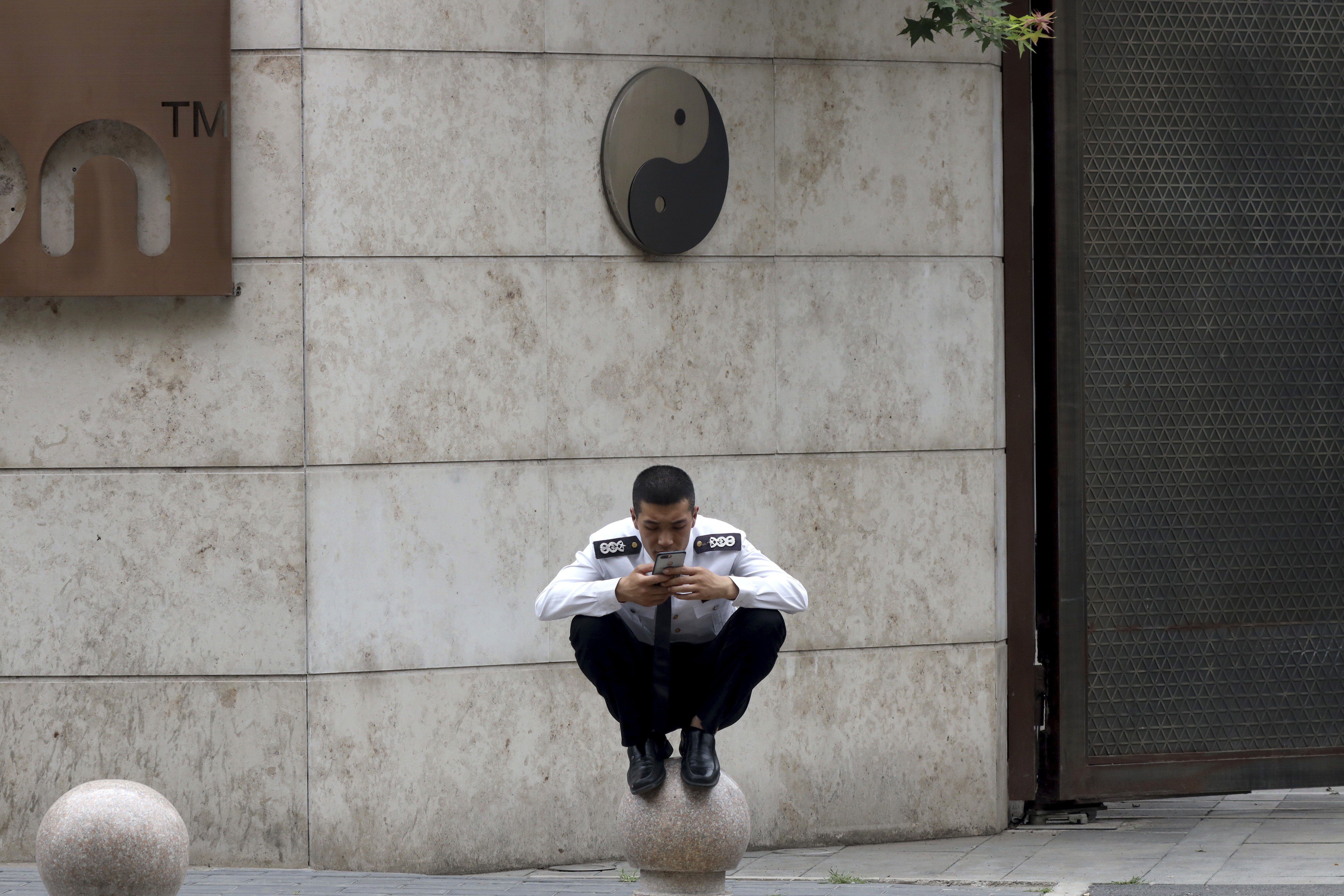 A security guard looks at his mobile phone while perched on a barrier near a yin and yang symbol in Beijing. The symbol is rooted in ancient Chinese philosophy and represents harmony. Photo: AP