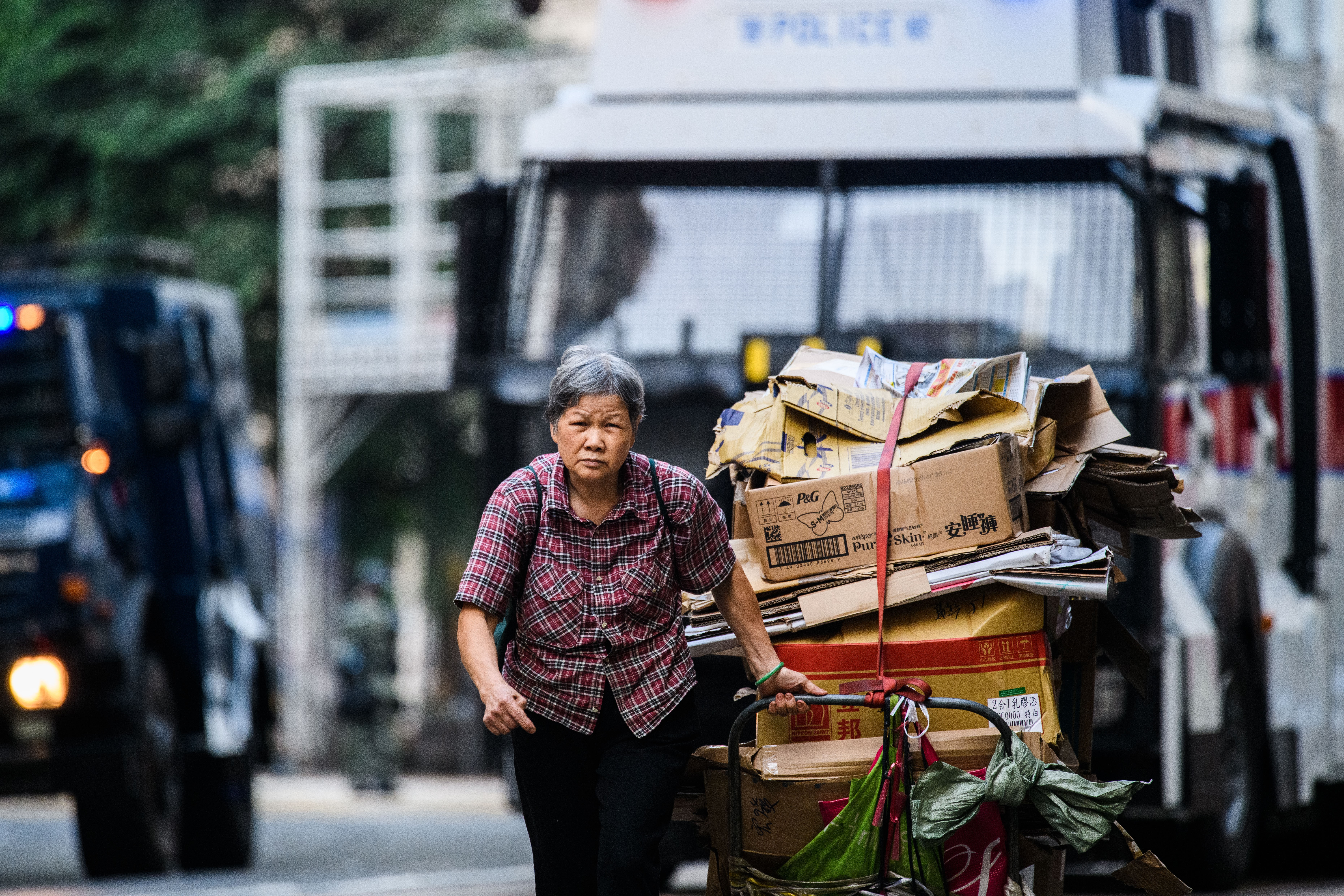 An elderly woman drags a trolley load of cardboard for recycling in front of a police water cannon vehicle in Hong Kong. Photo: AFP