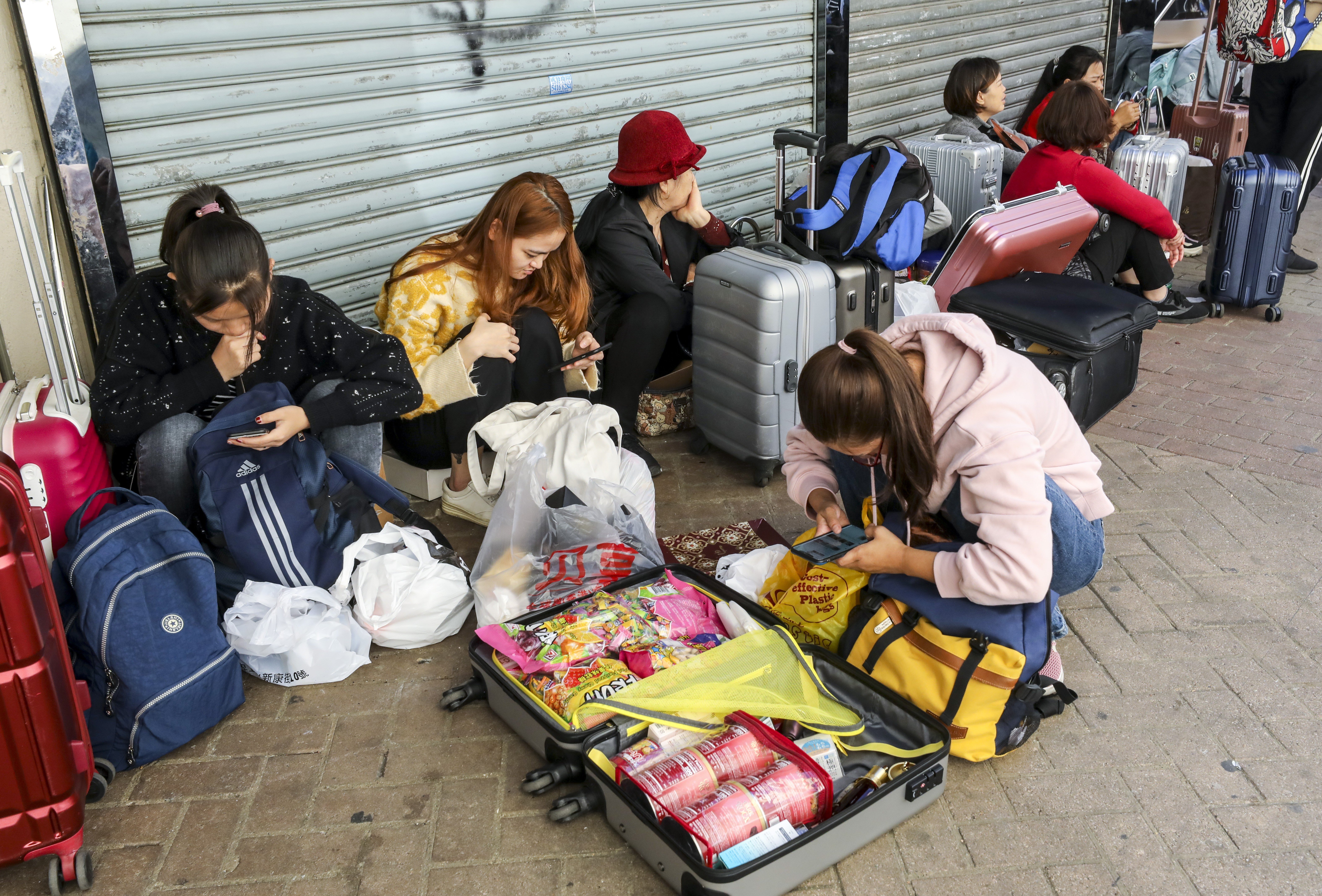 Mainland tourists with suitcases full of shopping sit on the pavement in Sheung Shui. Photo: Dickson Lee
