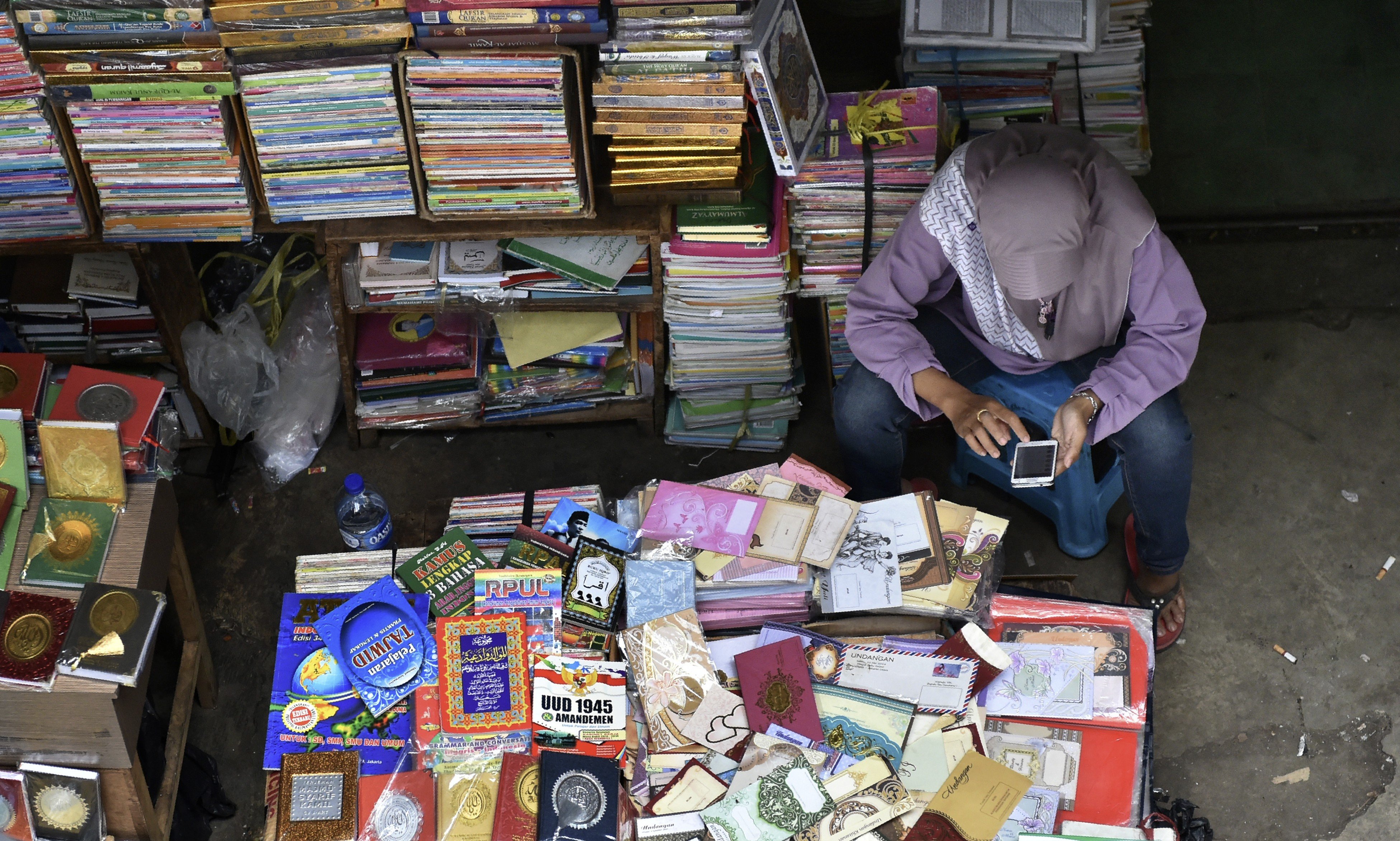 A book vendor in Jakarta uses her mobile phone while waiting for customers. Indonesia has one of the fastest growing internet penetration rates in the region. Photo: AFP
