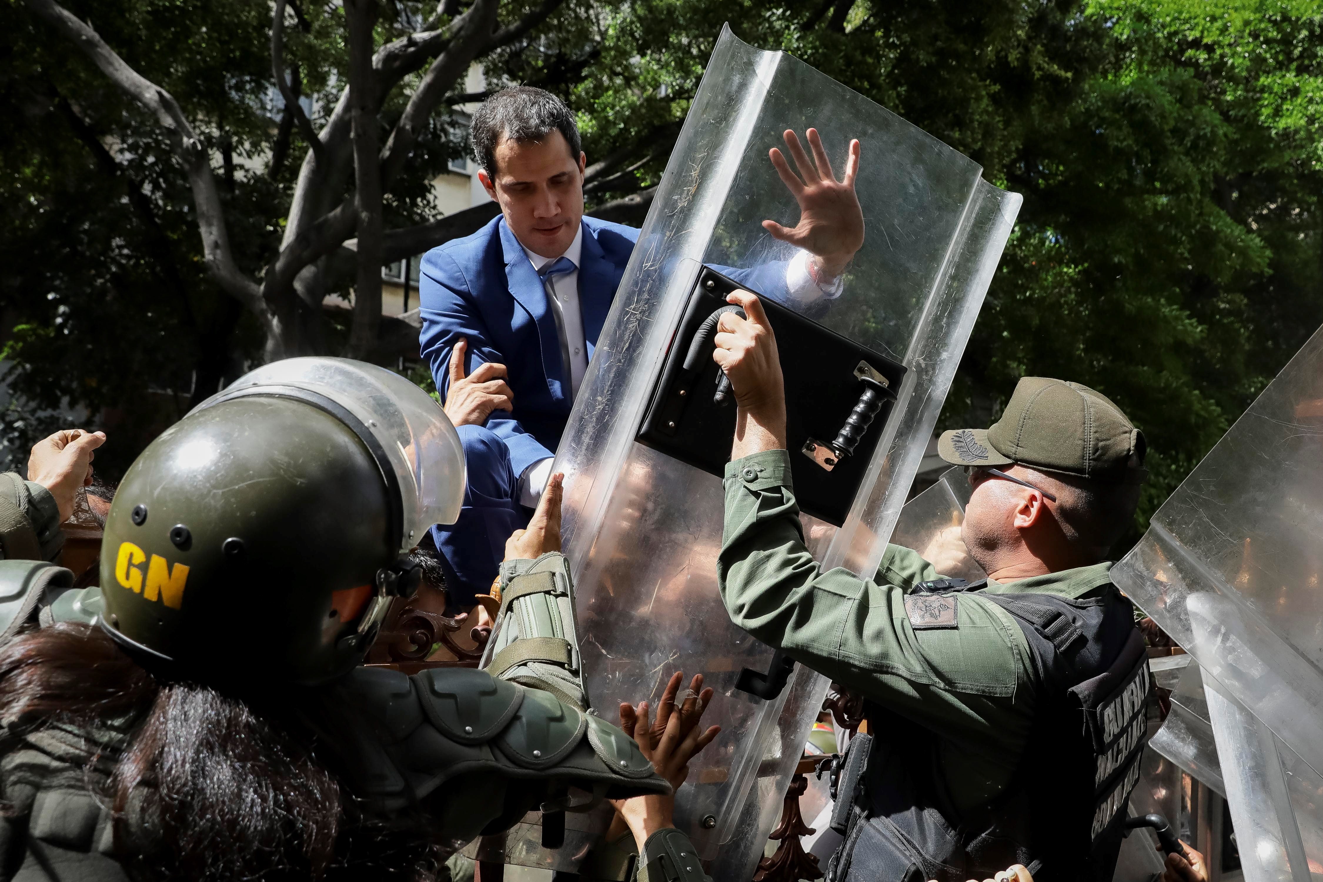 Venezuelan opposition leader Juan Guaido climbs a fence in an attempt to enter the headquarters of the National Assembly. Photo: EPA