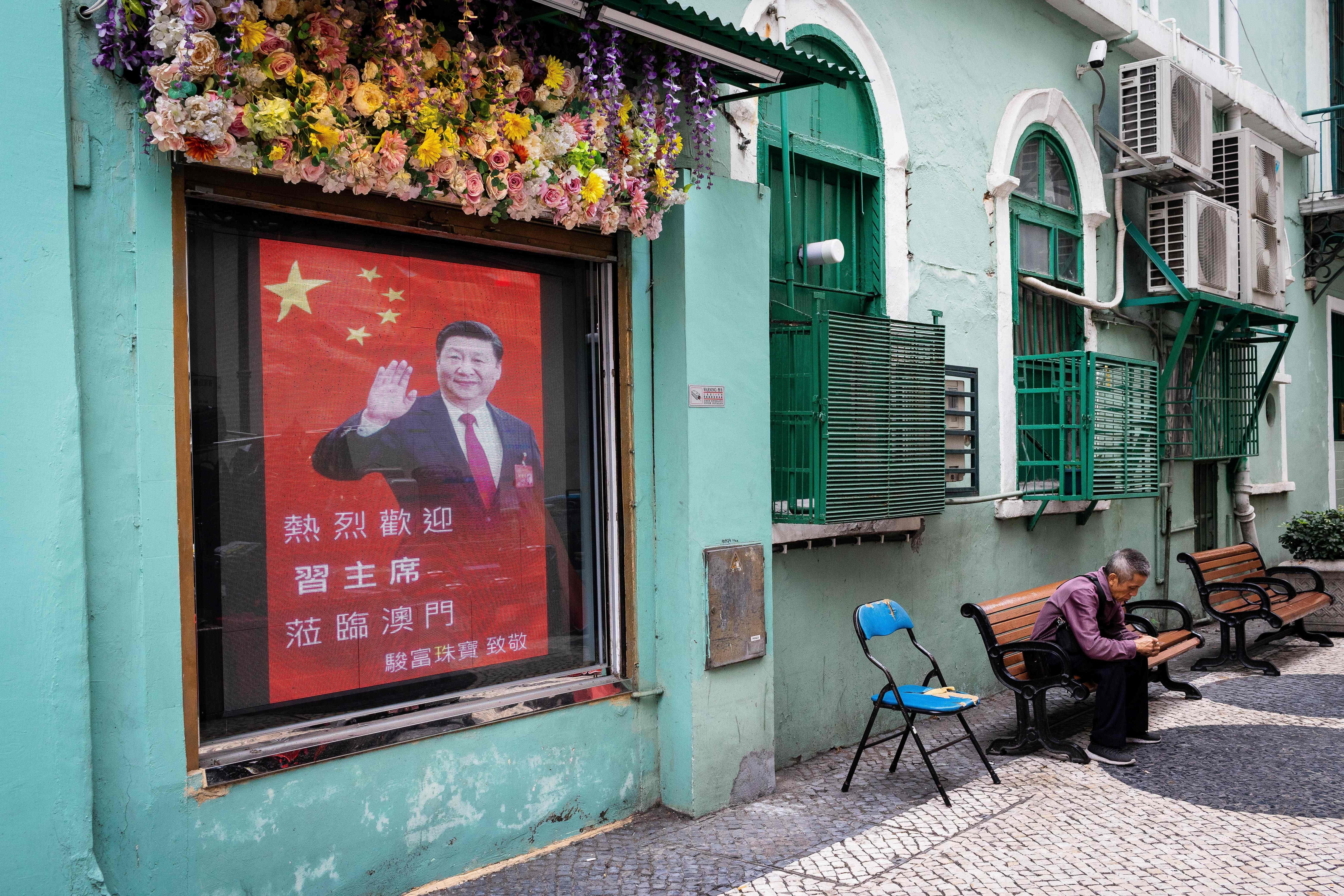 A man sits in an alley next to a screen with the image of China's President Xi Jinping in Macau on December 19, 2019 as the city marks the 20th anniversary of the handover from Portugal to China. Photo: AFP