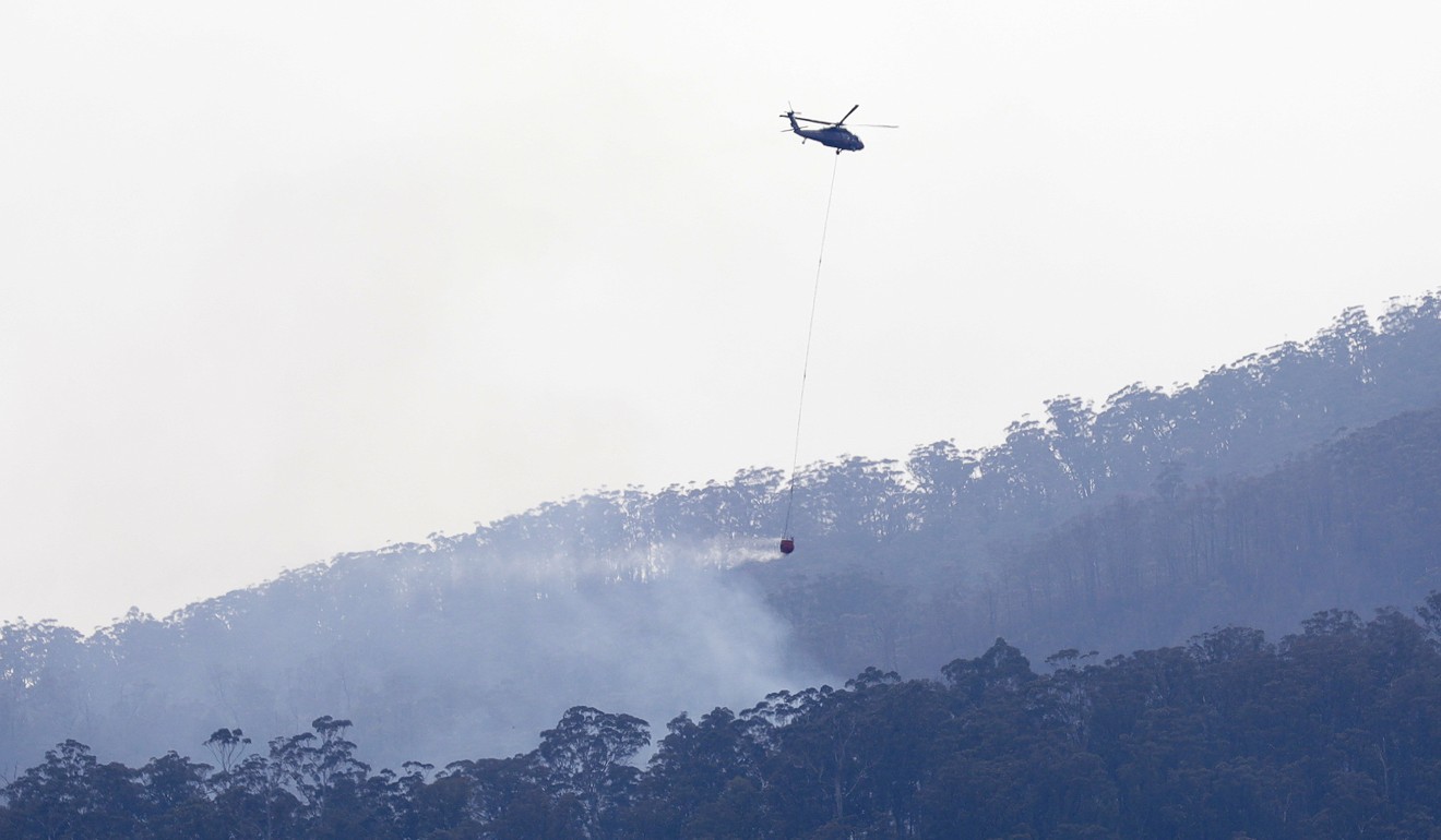 A helicopter prepares to drop water on a bush fire near Cobargo. Photo: AP