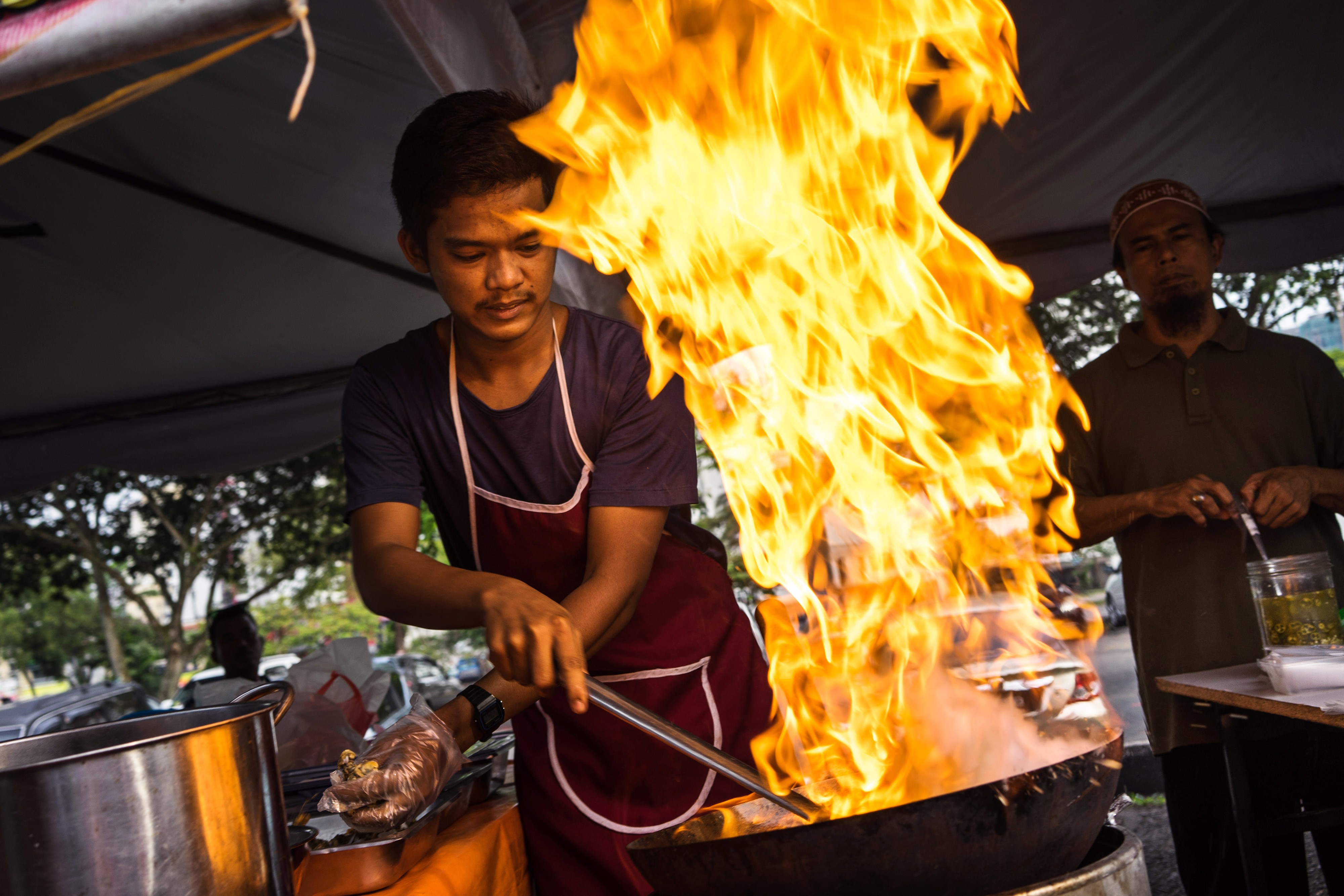 Flames rise from a wok while a chef cooks fried noodles at a food stall in a market in Johor Bahru, Johor, Malaysia on Friday, July 10, 2015. Photographer: Sanjit Das/Bloomberg