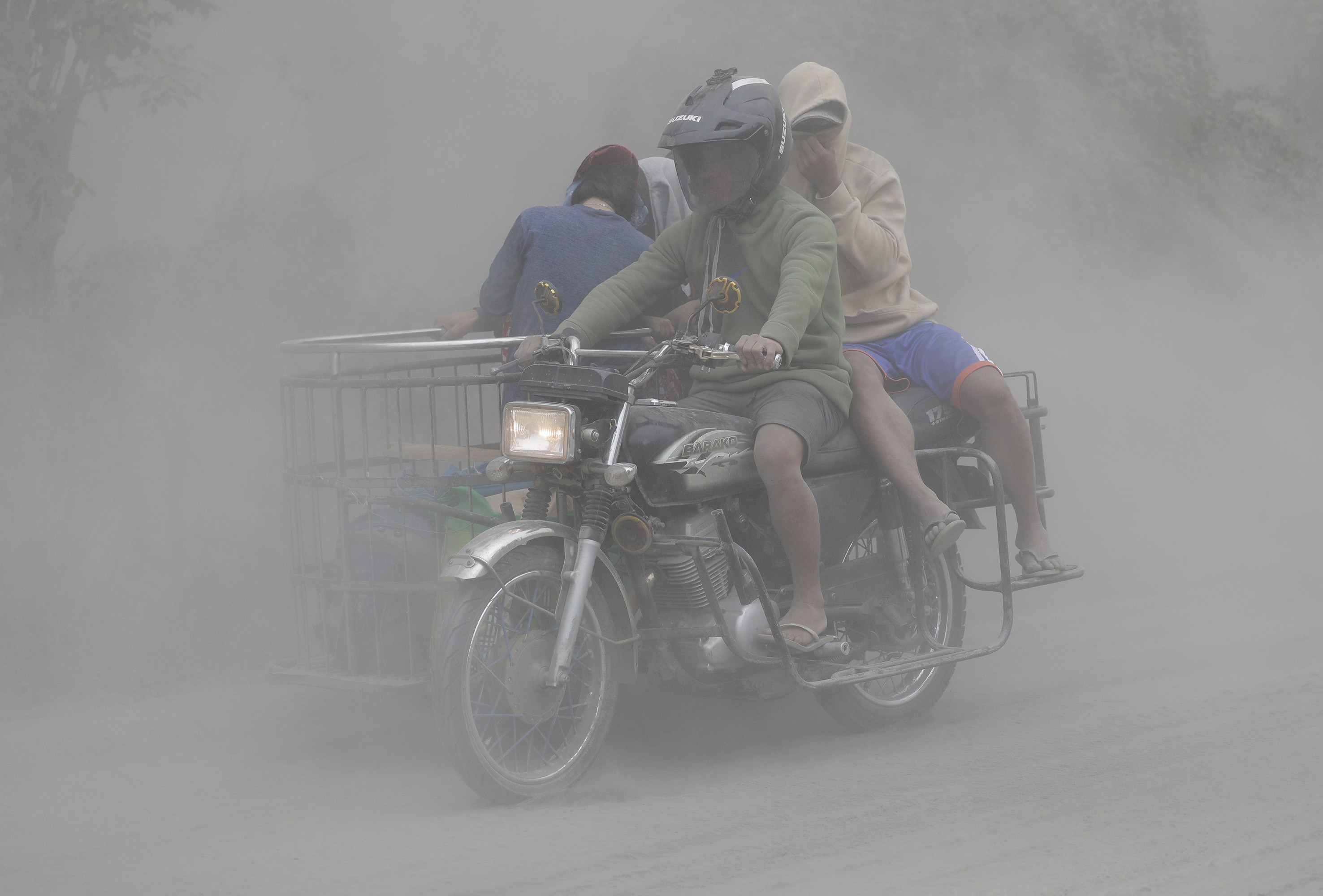 In this Jan. 13, 2020, photo, a family rides their motorcycle through clouds of ash as they evacuate to safer grounds as Taal volcano in Tagaytay, Cavite province, southern Philippines. Red-hot lava is gushing from the volcano after a sudden eruption of ash and steam that forced residents to flee and shut down Manila’s airport, offices and schools. (AP Photo/Aaron Favila, File)