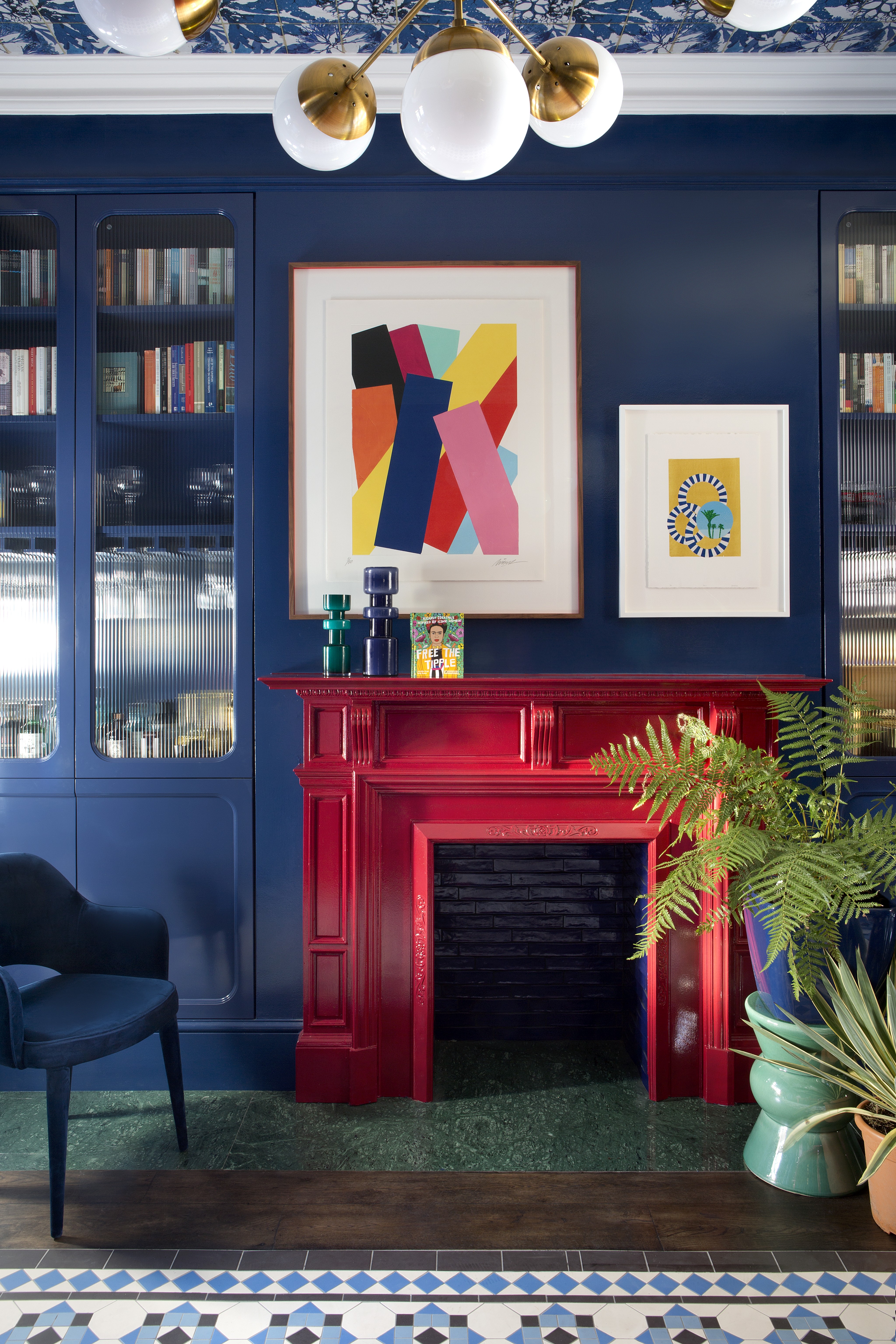A fireplace in bright red and colourful artworks complement the wide swathe of blue wall and shelves. Photo: Barbara Corsico/Living Inside