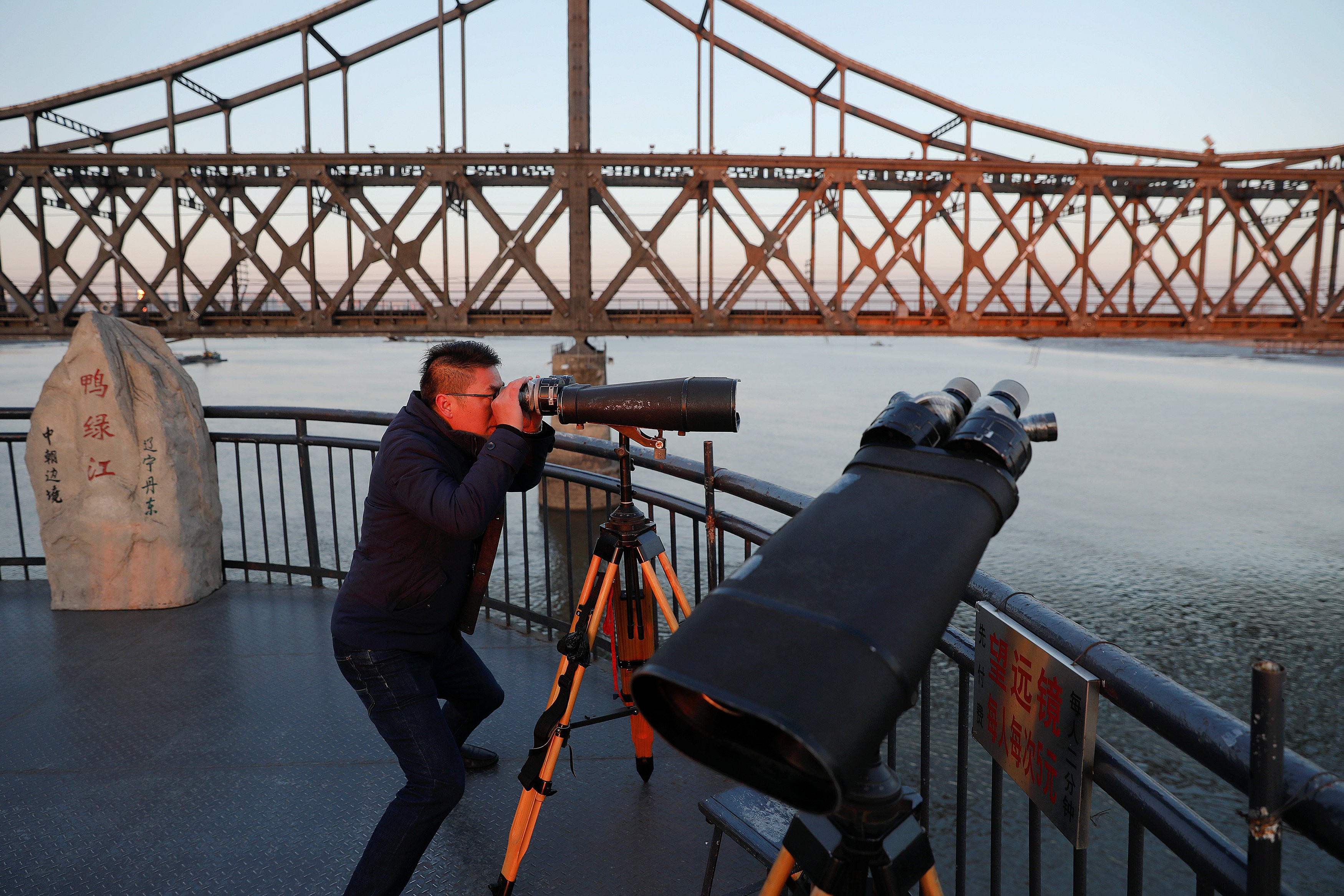 A man looks through binoculars towards North Korea on the Broken Bridge over the Yalu River that connects the North Korean town of Sinuiju and Dandong in Liaoning Province, China. Photo: Reuters
