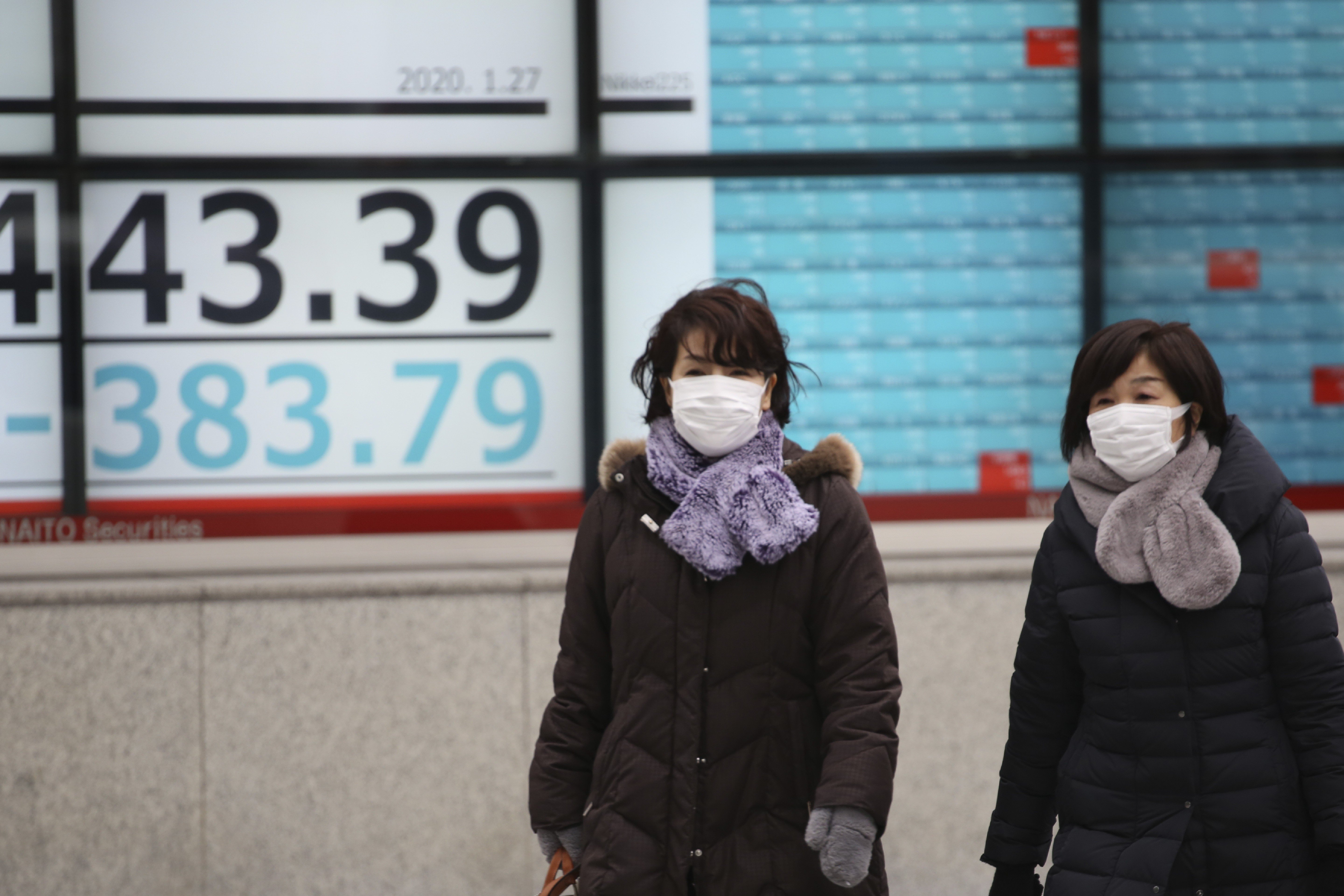 People walk by an electronic stock board of a securities firm in Tokyo on January 27. Shares tumbled in the few Asian markets open as China announced sharp increases in the number of people affected by an outbreak of a new coronavirus. Photo: AP