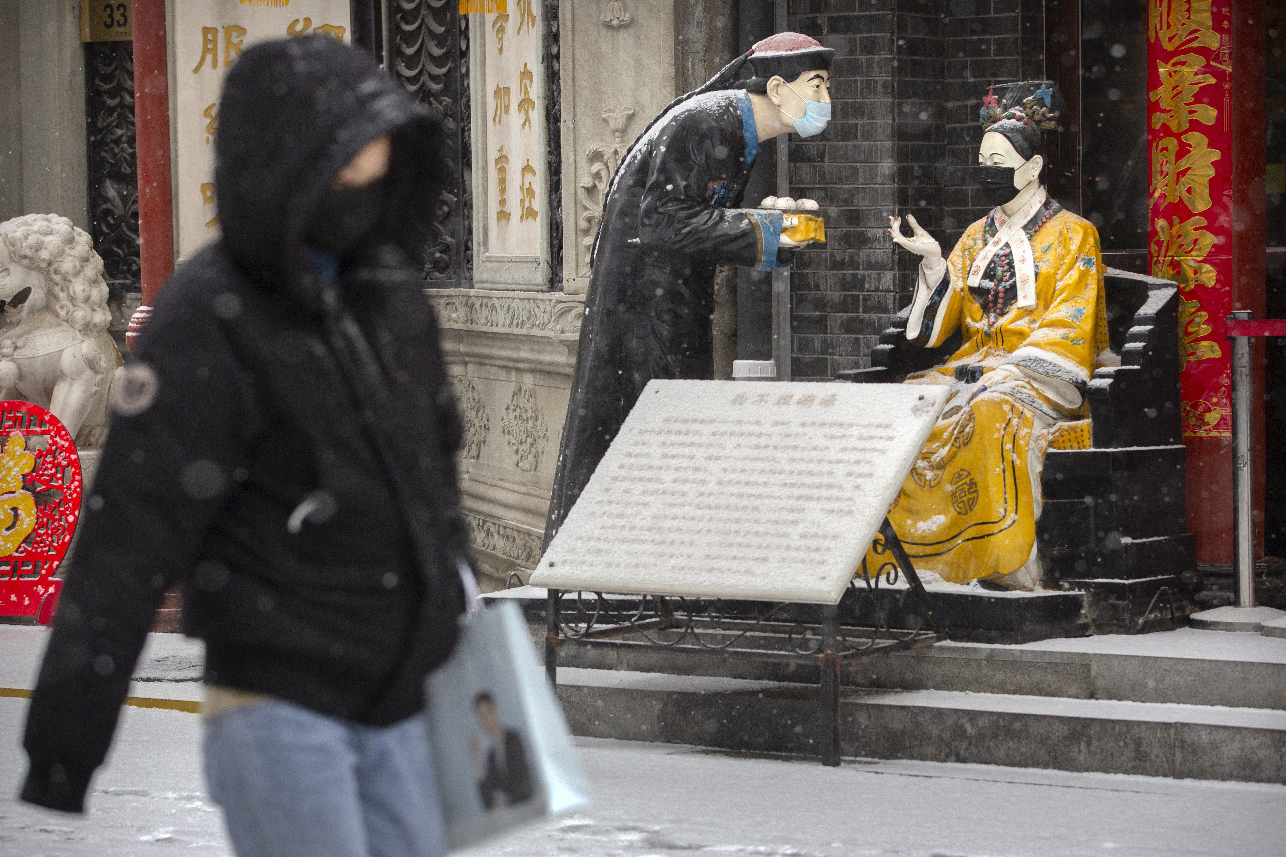 A woman walks past statues wearing face masks, as the snow falls in Beijing on February 5. Photo: AP