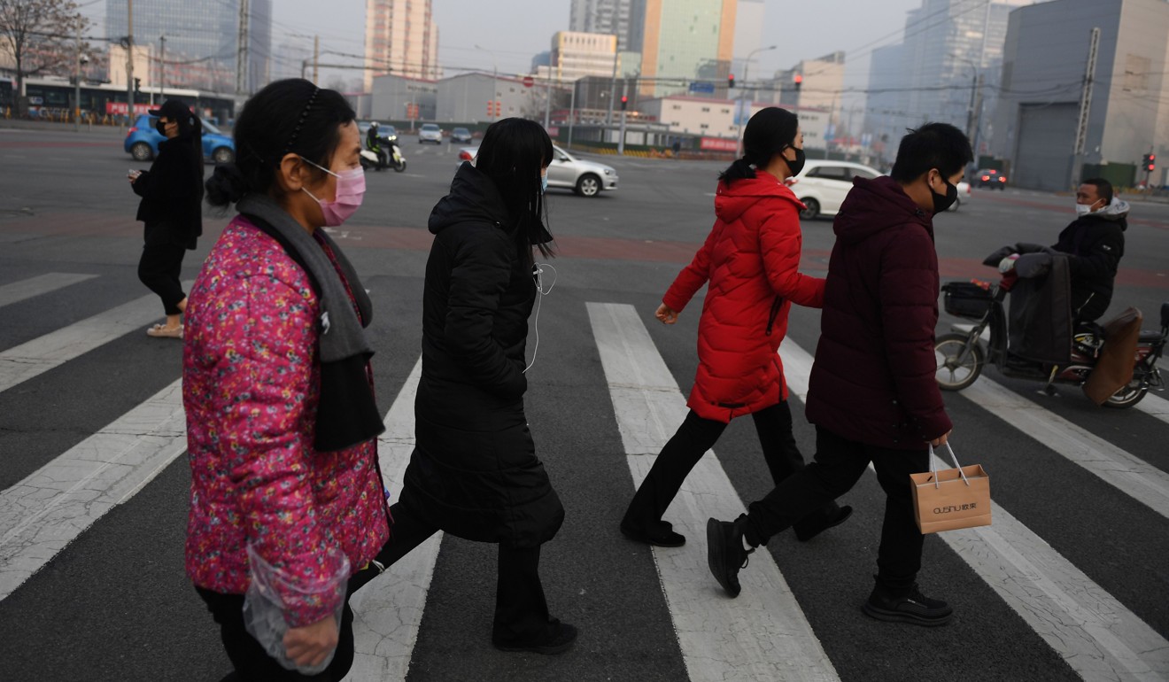 People wear face masks as they cross a normally busy street in Beijing on Tuesday. Photo: AFP