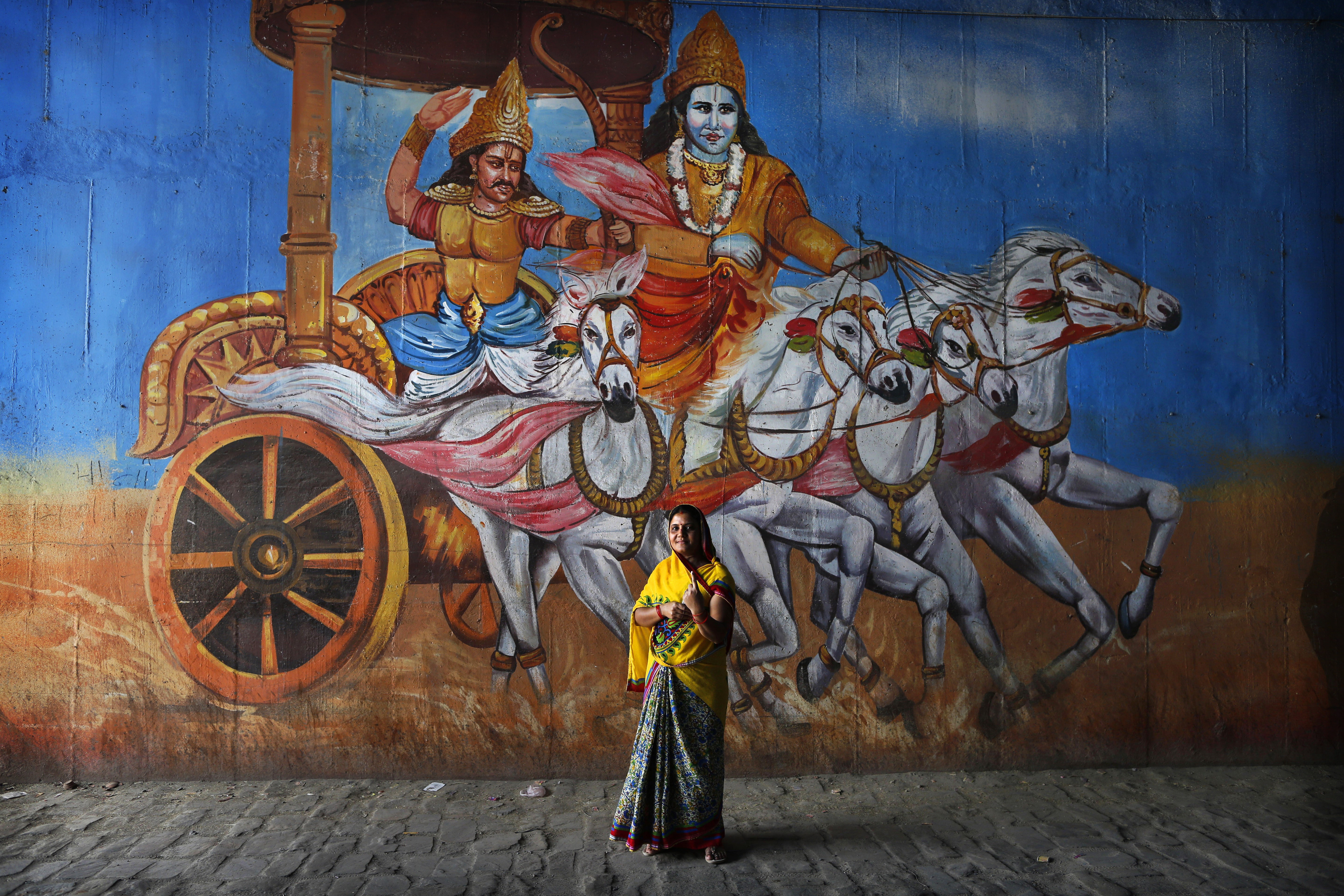 An Indian woman stands in front of a mural depicting a scene from the Hindu epic Mahabharata, as she displays an indelible ink mark on her finger, proof of having cast her vote in national elections, on May 12, 2019, in Prayagraj in the northern state of Uttar Pradesh. Photo: AP