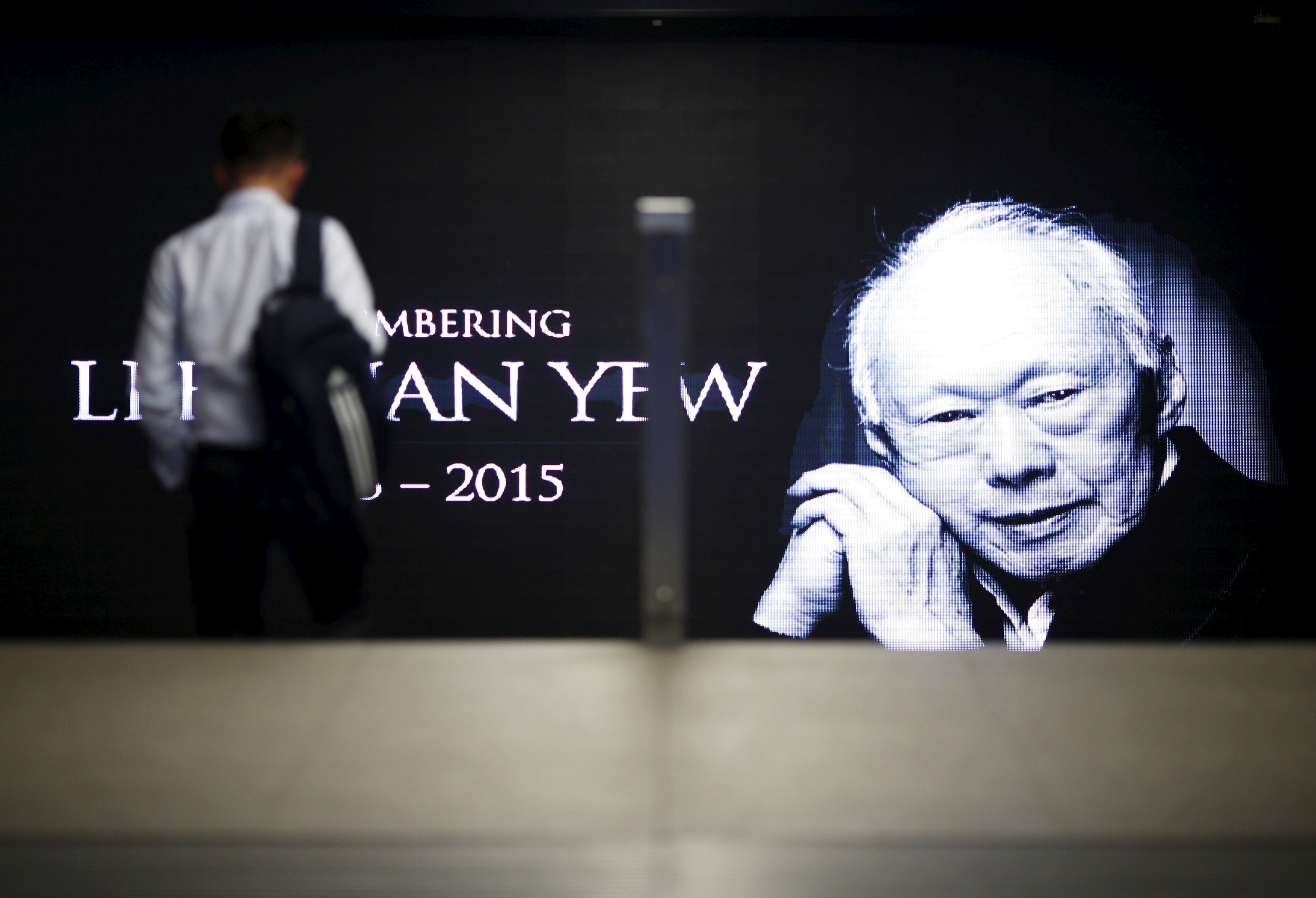 A commuter passes a signboard bearing an image of Lee Kuan Yew, the first prime minister of Singapore. Photo: Reuters