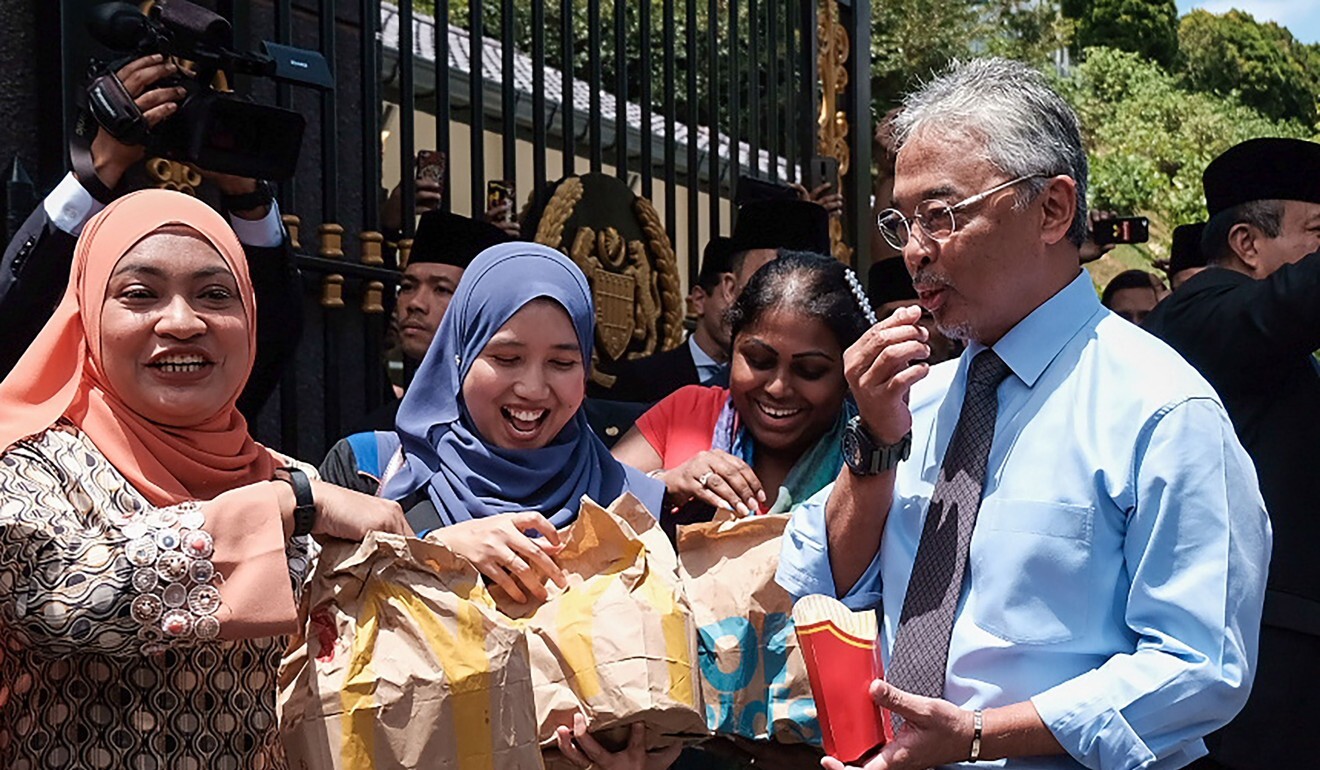 Malaysia’s King Sultan Abdullah hands out packages of fast food to reporters outside the National Palace in Kuala Lumpur. Photo: AFP