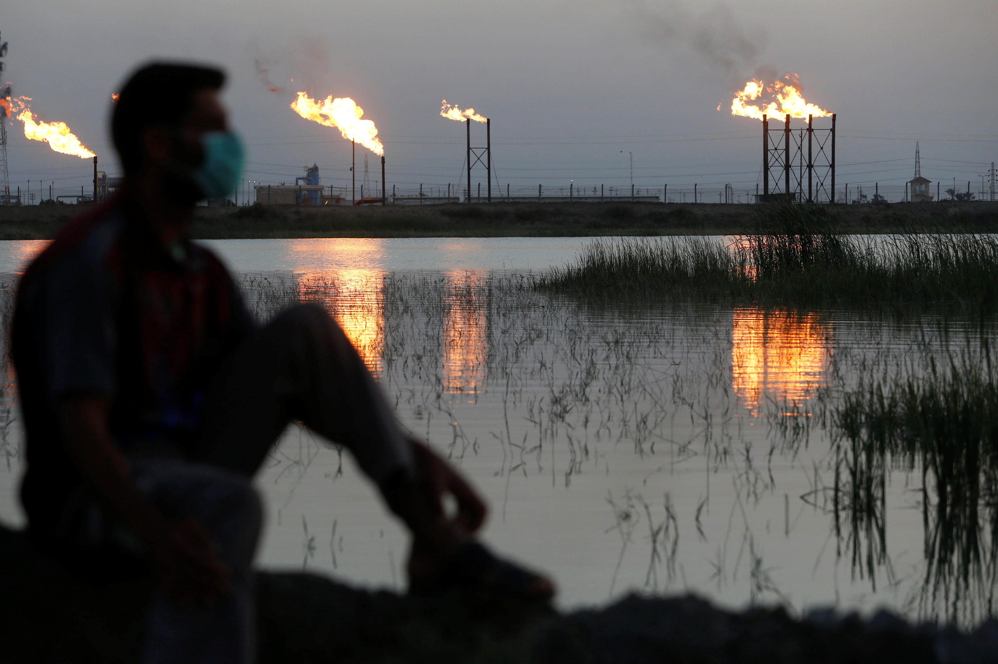 Flames emerge from flare stacks at an oilfield in Iraq behind a man wearing a face mask as protection against coronavirus. Photo: Reuters