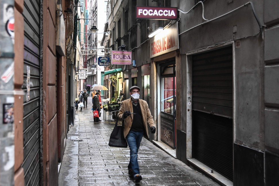 A resident wearing a mask walks past shops in Genoa, Italy. Photo: AFP